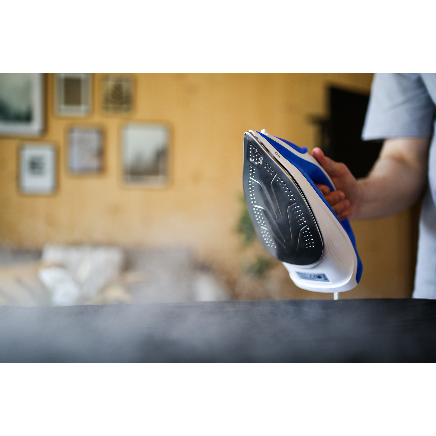 Iron with steam over a black surface. Person holding the iron in the background.