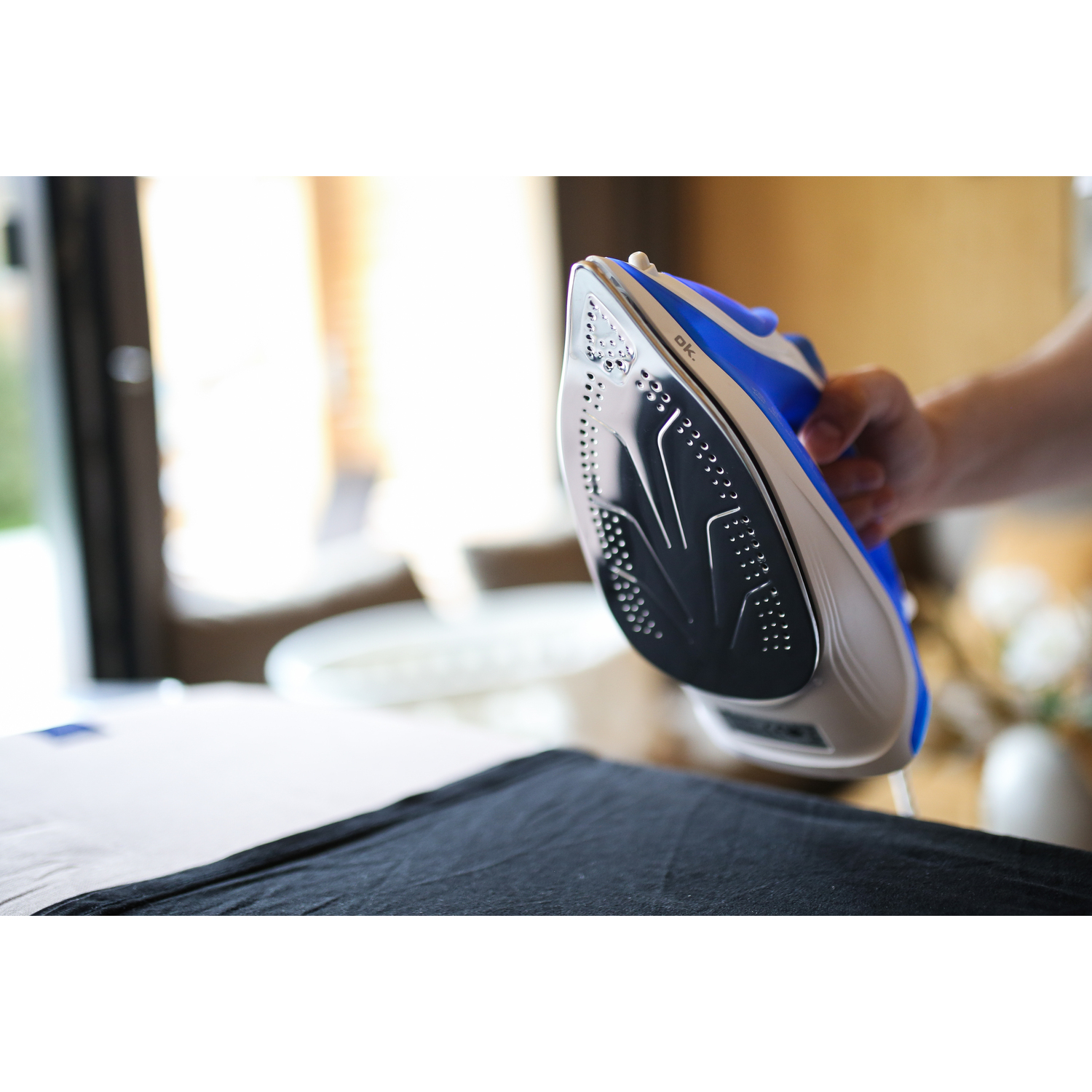 Ironing iron in use. A hand holding the iron over a black cloth.