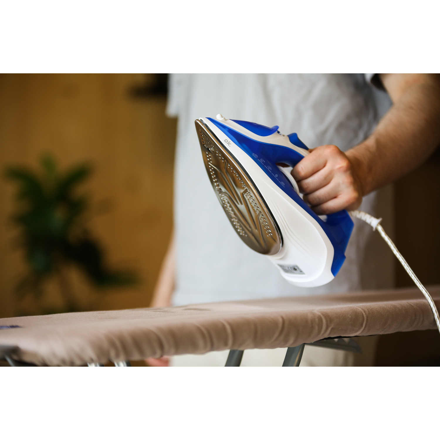 A person ironing clothes with a blue and white iron. The iron is on an ironing board.