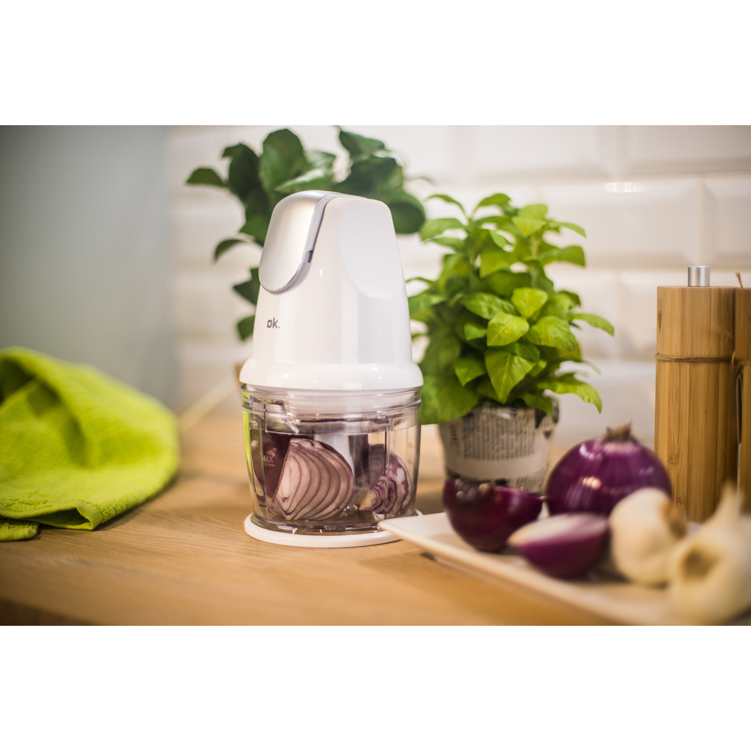 Witte voedselhakker met rode uien erin, omringd door planten en ingrediënten.