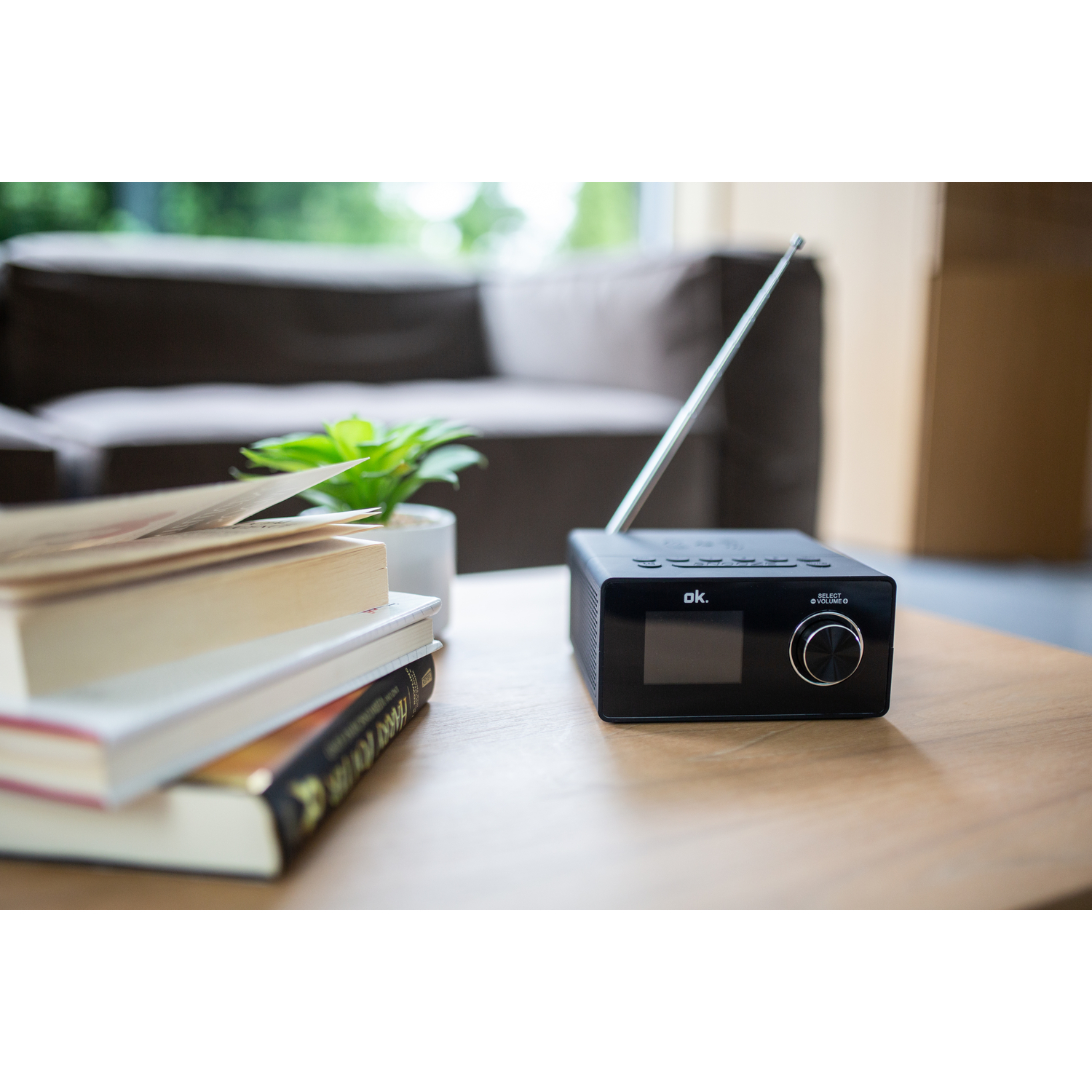 Une radio noire sur une table en bois avec des livres et une plante en arrière-plan.