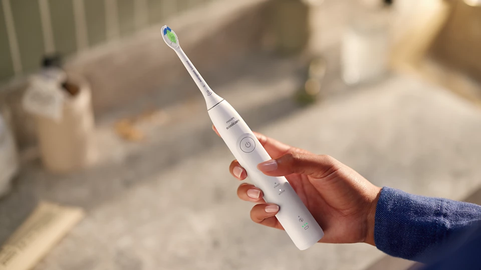 La mano di una persona che tiene uno spazzolino Philips Sonicare bianco vicino a un lavandino.