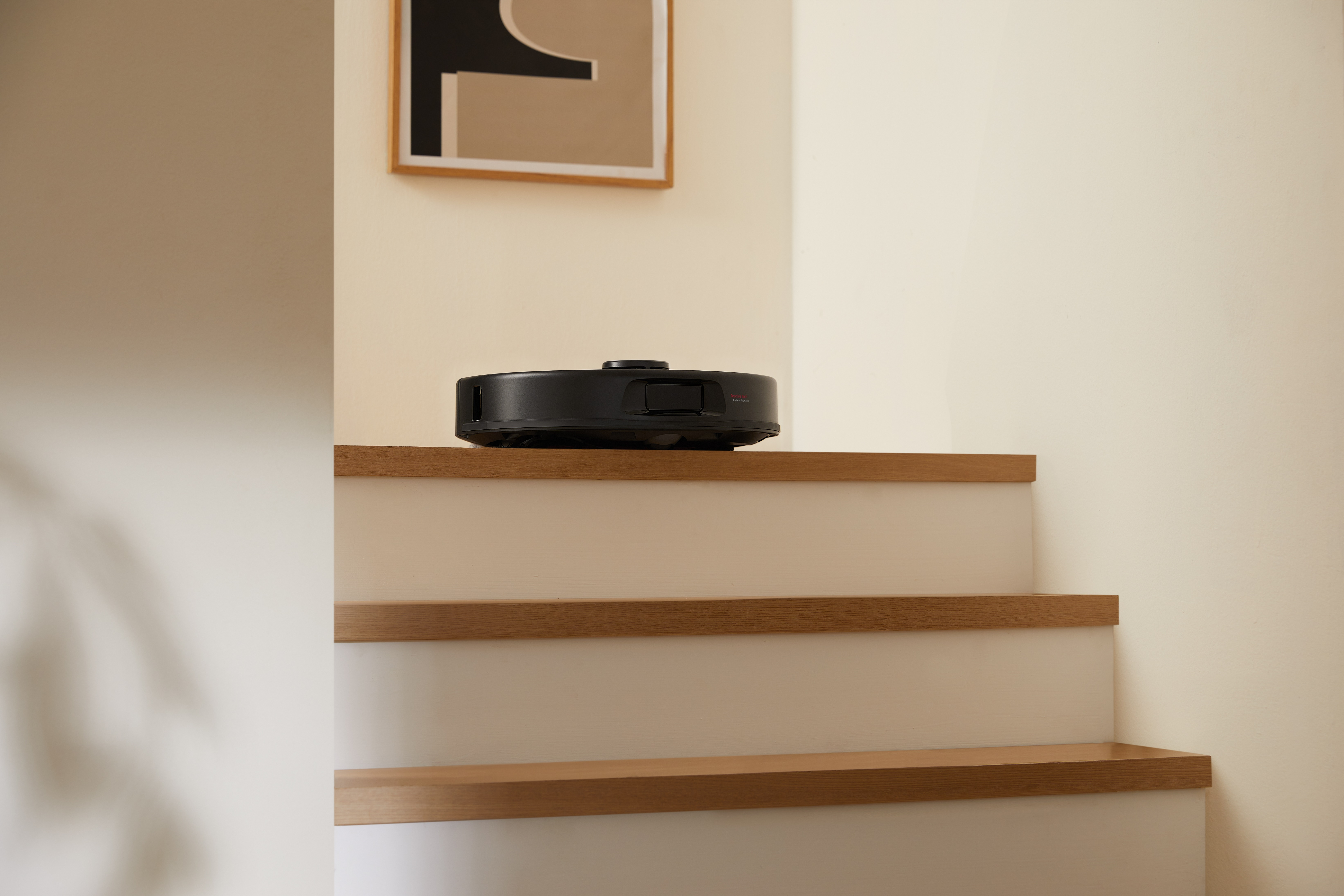 Czarny robot odkurzający jest na schodach. Obraz wisi na ścianie w tle.
