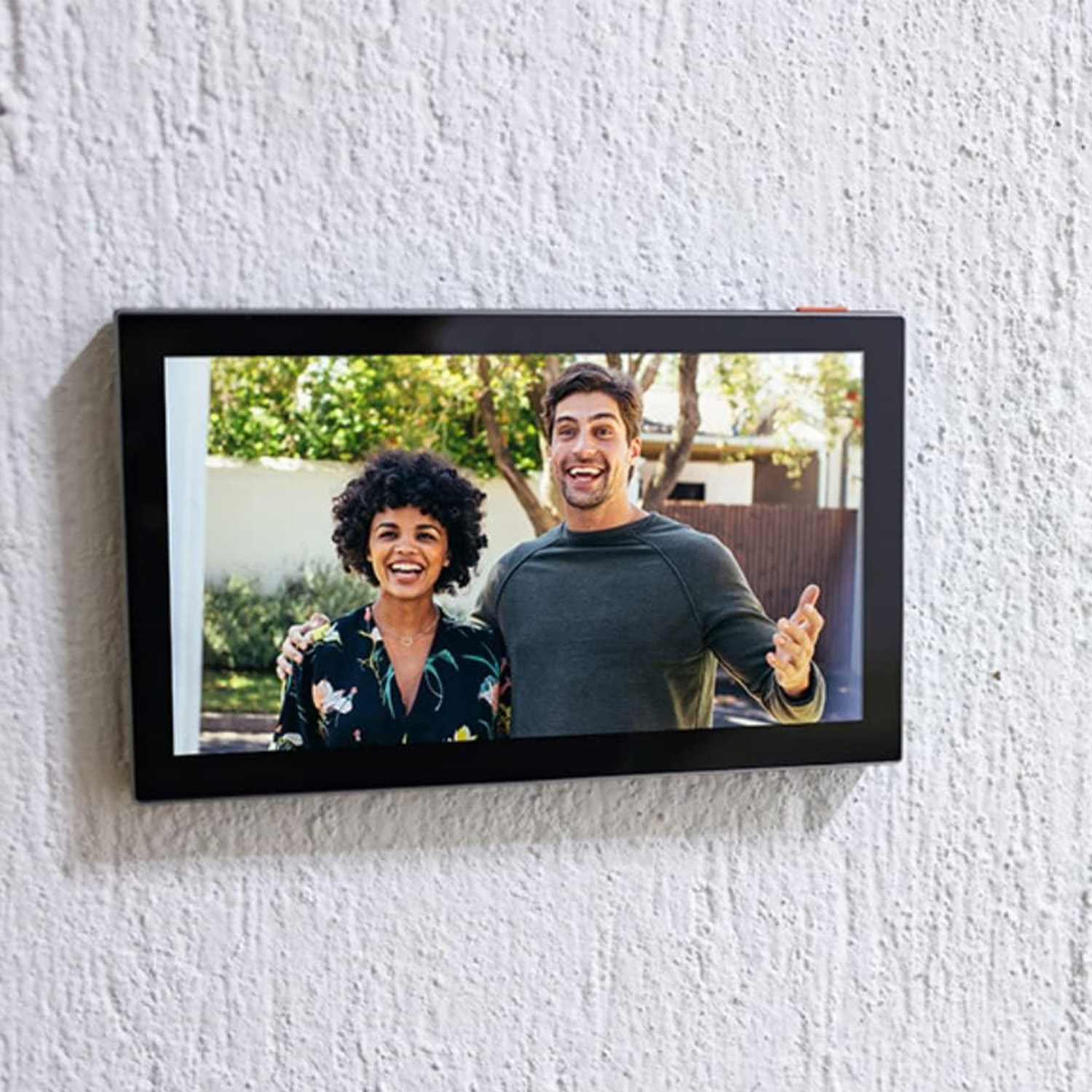 Una foto è sul muro. Una coppia sorridente è nella foto. Lo sfondo è una casa.