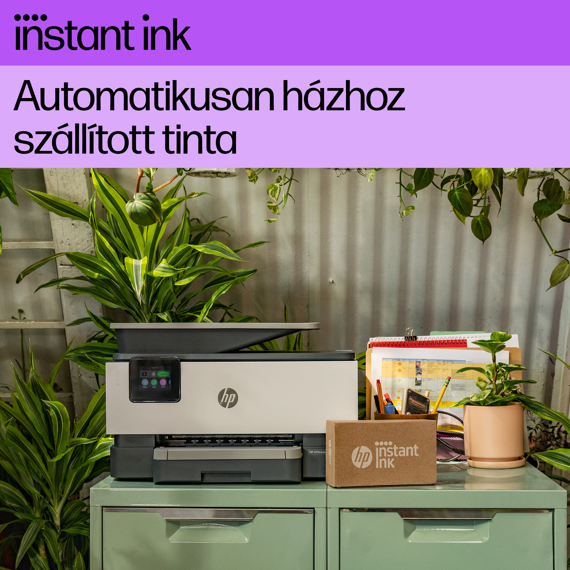 Egy nyomtató egy mentazöld szekrényen, rajta egy 'instant ink' feliratú dobozzal és növényekkel körülvéve.