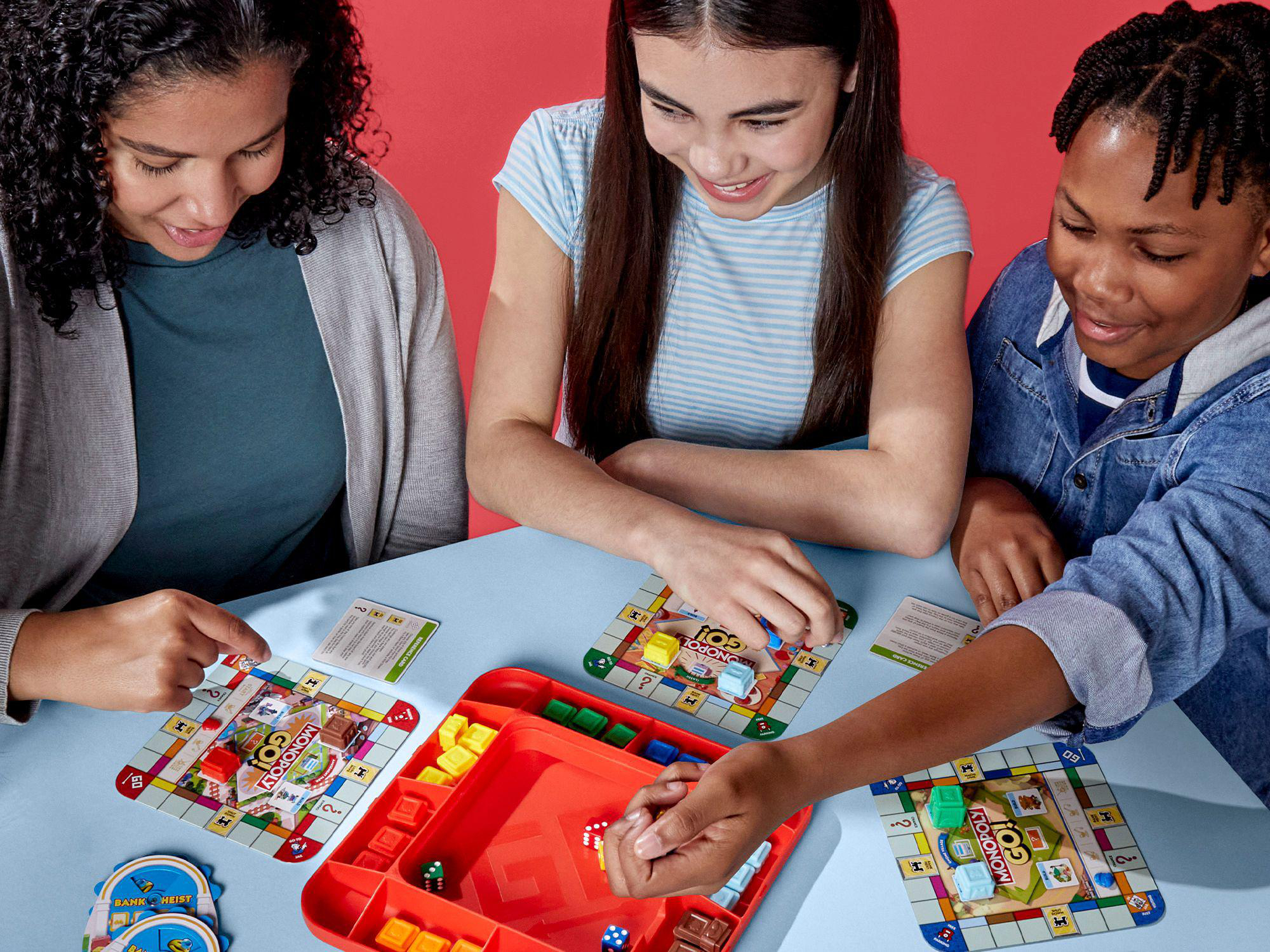 Drei Personen spielen Monopoly Go!, buntes Spielbrett.