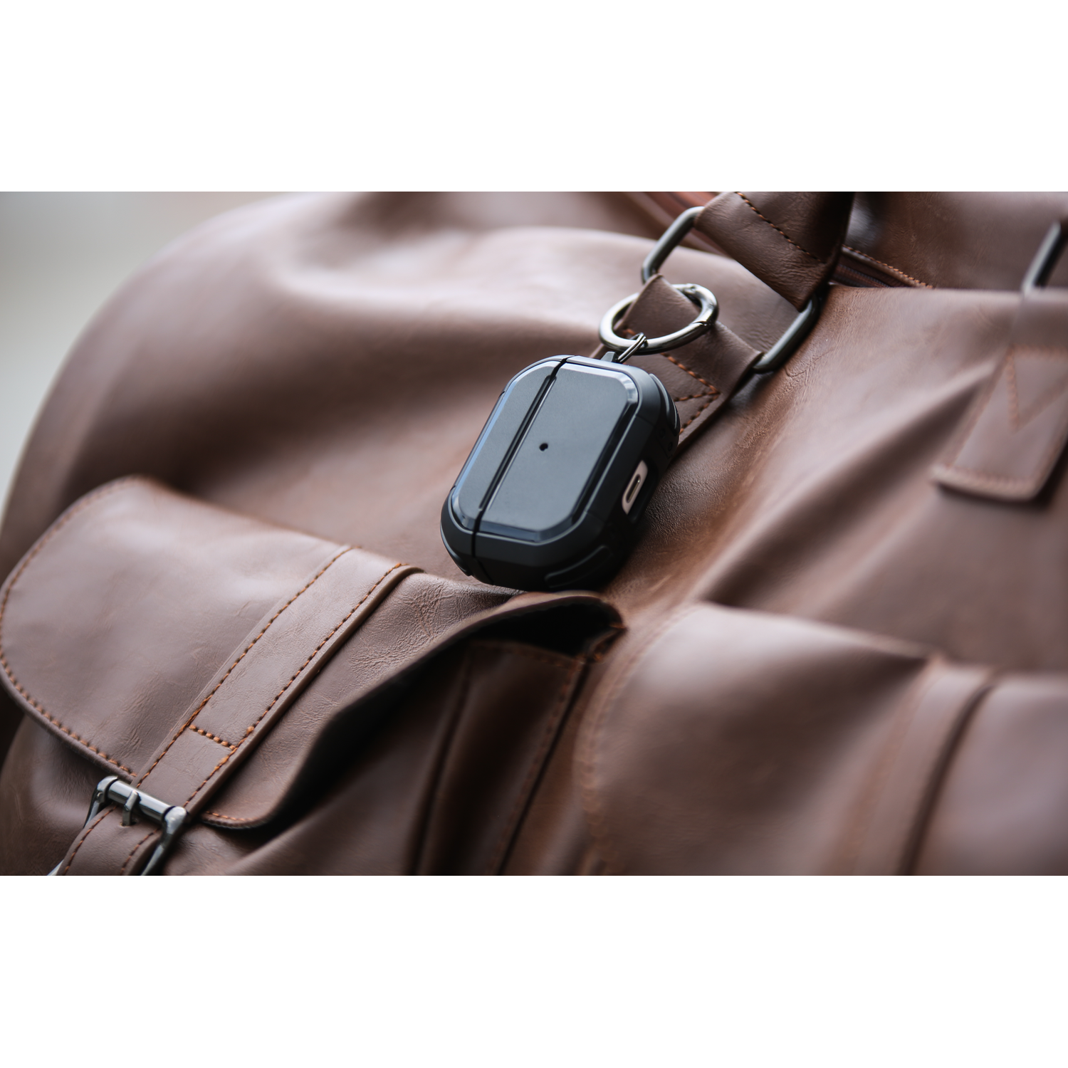 Een zwarte AirPods-hoes hangt aan een bruine leren tas.