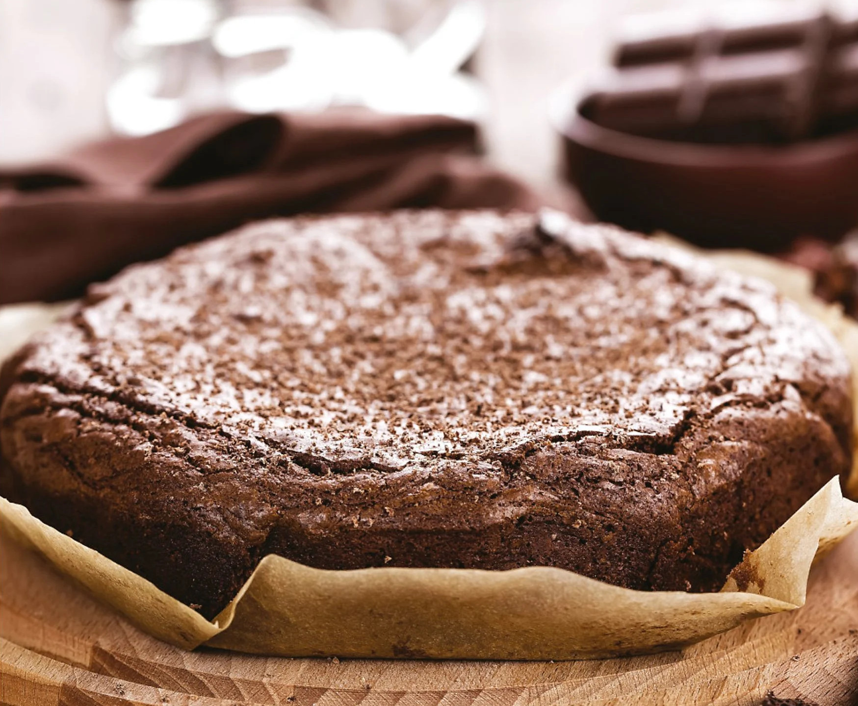 Okrągłe ciasto czekoladowe z cukrem pudrem na drewnianej desce.