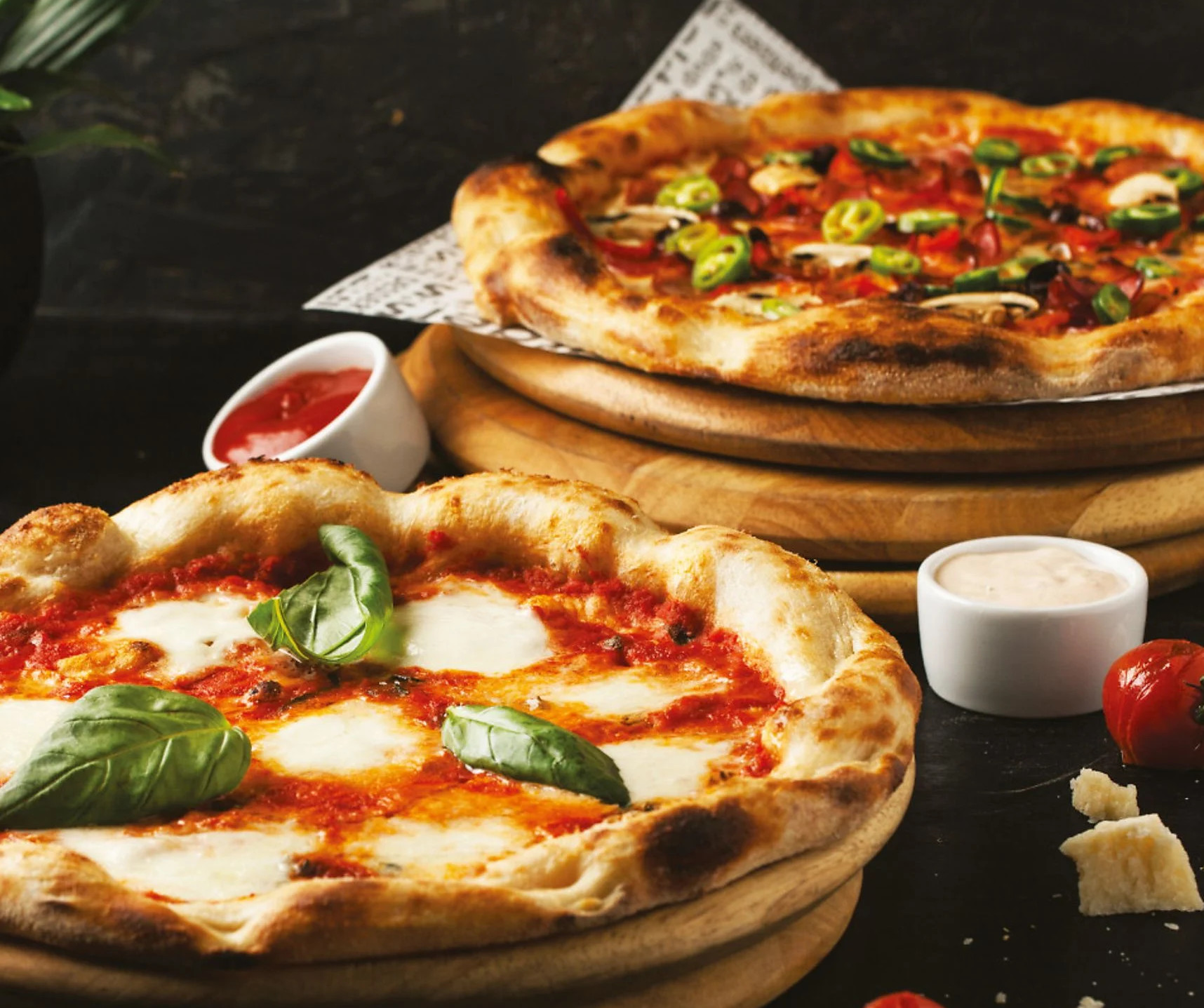 Dwie pizze z różnymi dodatkami. Jedna ma bazylię. Są sosy.