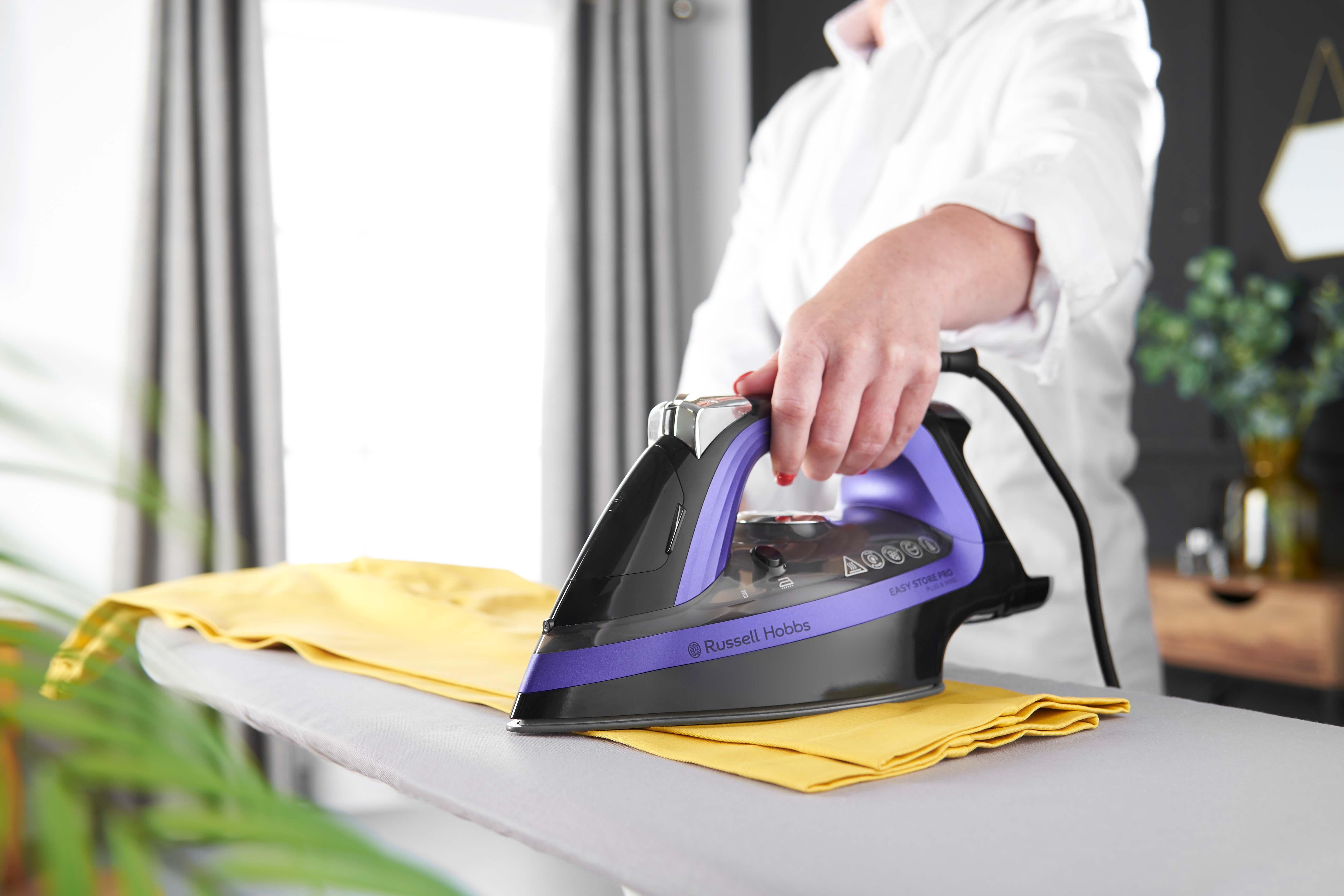 Osoba prasuje żółtą koszulę na desce do prasowania. Żelazko jest czarne i fioletowe.