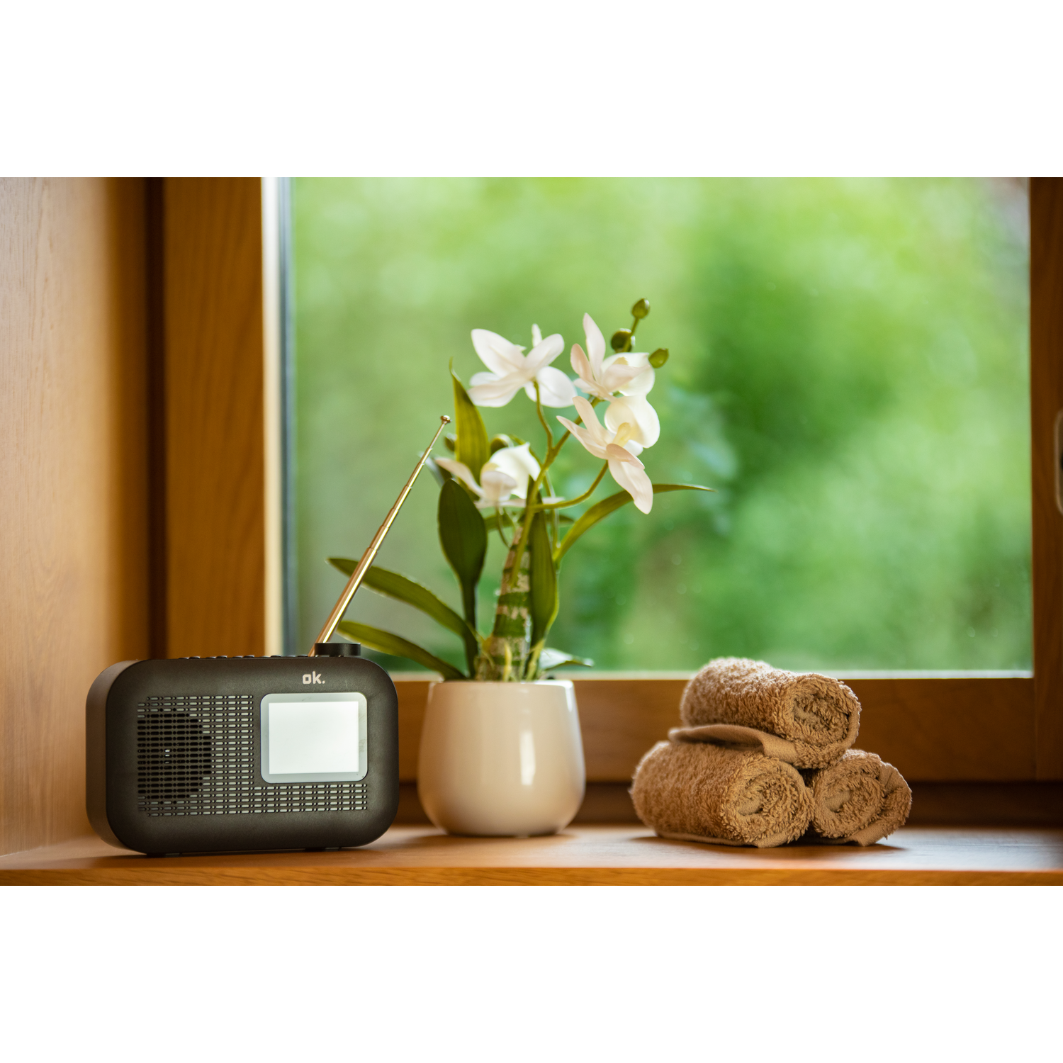 A small radio on a windowsill. A plant and towels are also there.