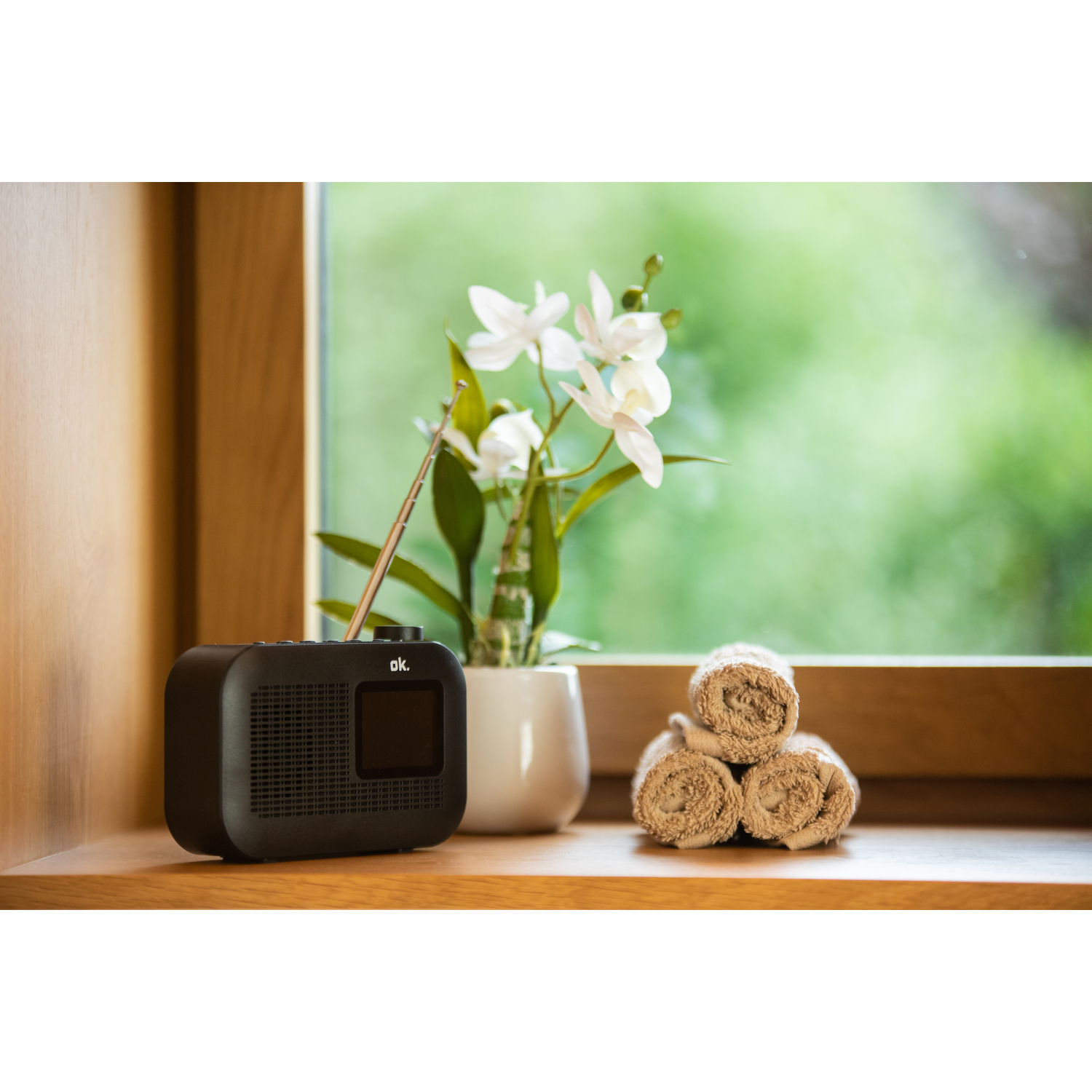 A black radio on a wooden shelf with flowers and towels.