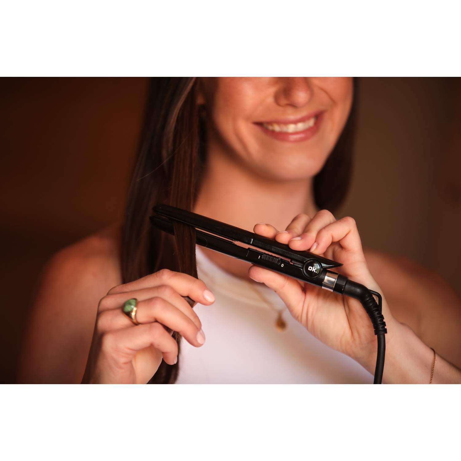 Woman using a black hair straightener, smiling, gold ring.