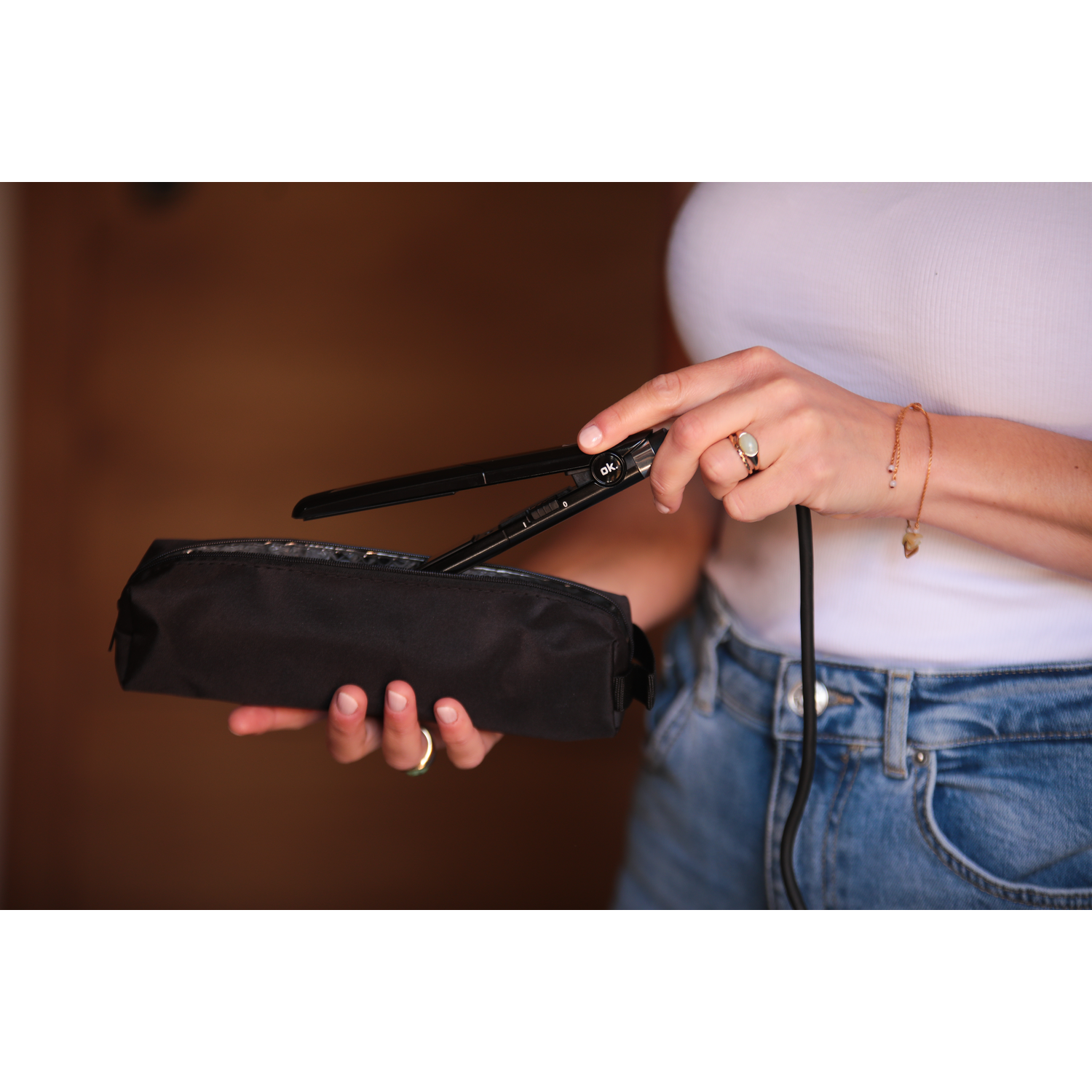 A woman's hands placing a hair straightener into a black travel case.