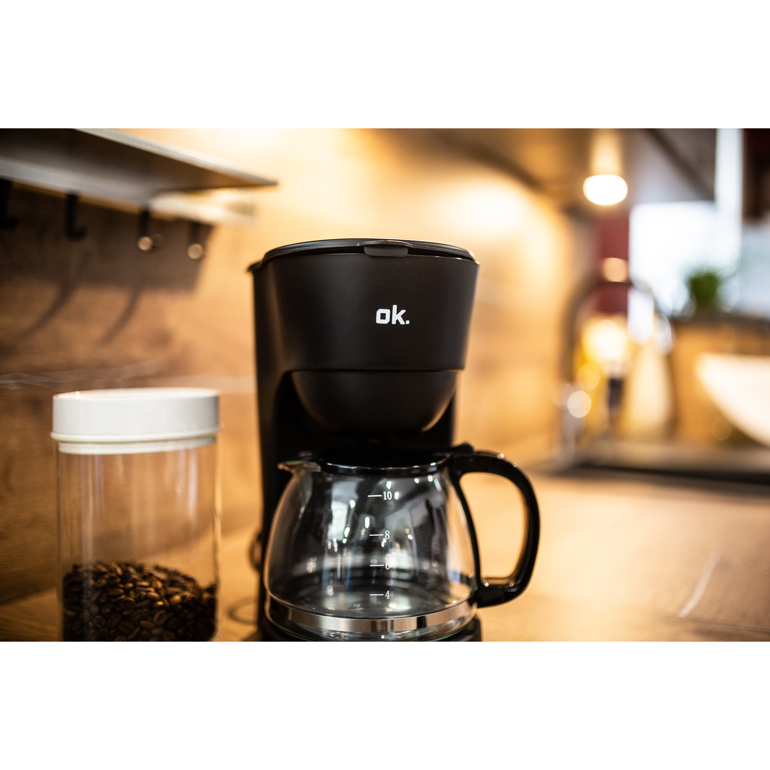 A black coffee maker with a glass carafe and coffee beans in a jar. Wooden background.