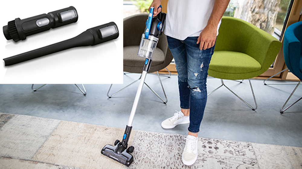 Mężczyzna odkurzający dywan. Części odkurzacza są w rogu. W pokoju znajdują się meble.