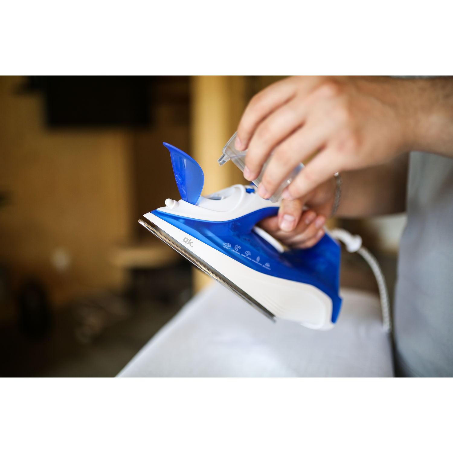 A person filling a blue and white iron with water, on an ironing board.