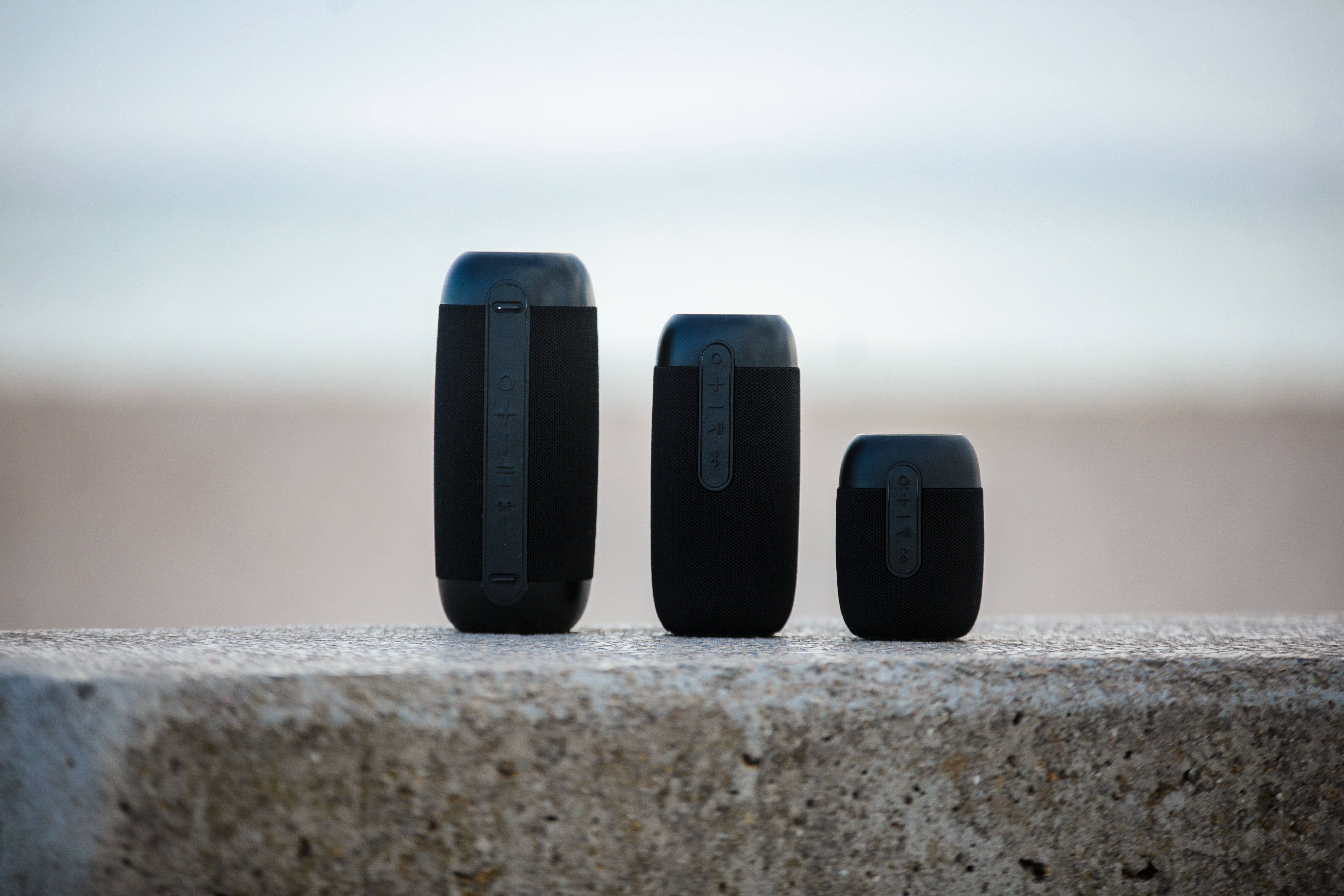 Trzy czarne głośniki przenośne o różnych rozmiarach na betonowej powierzchni.