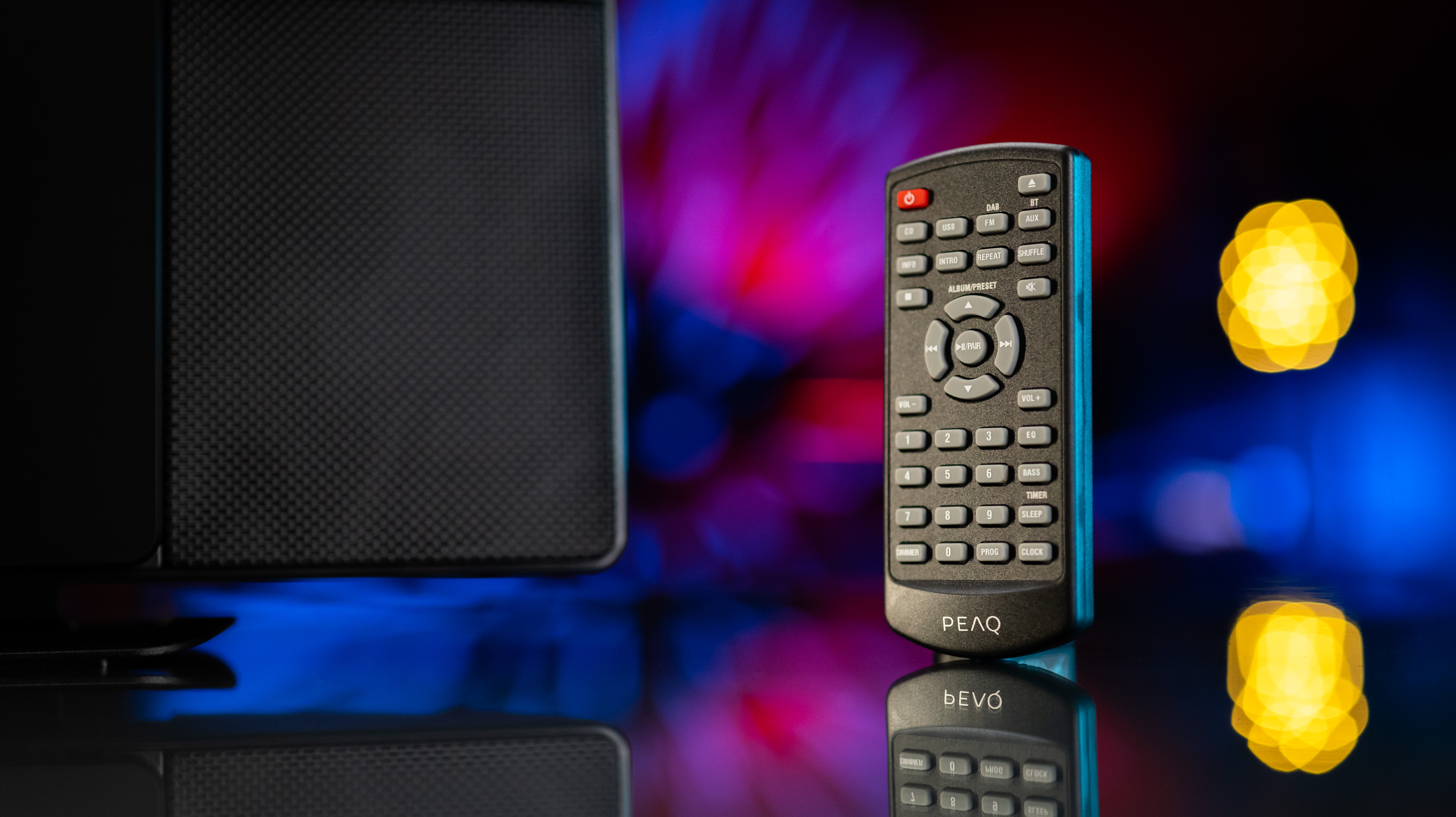 Czarny pilot z przyciskami, głośnik i światła bokeh w ciemnej scenie.