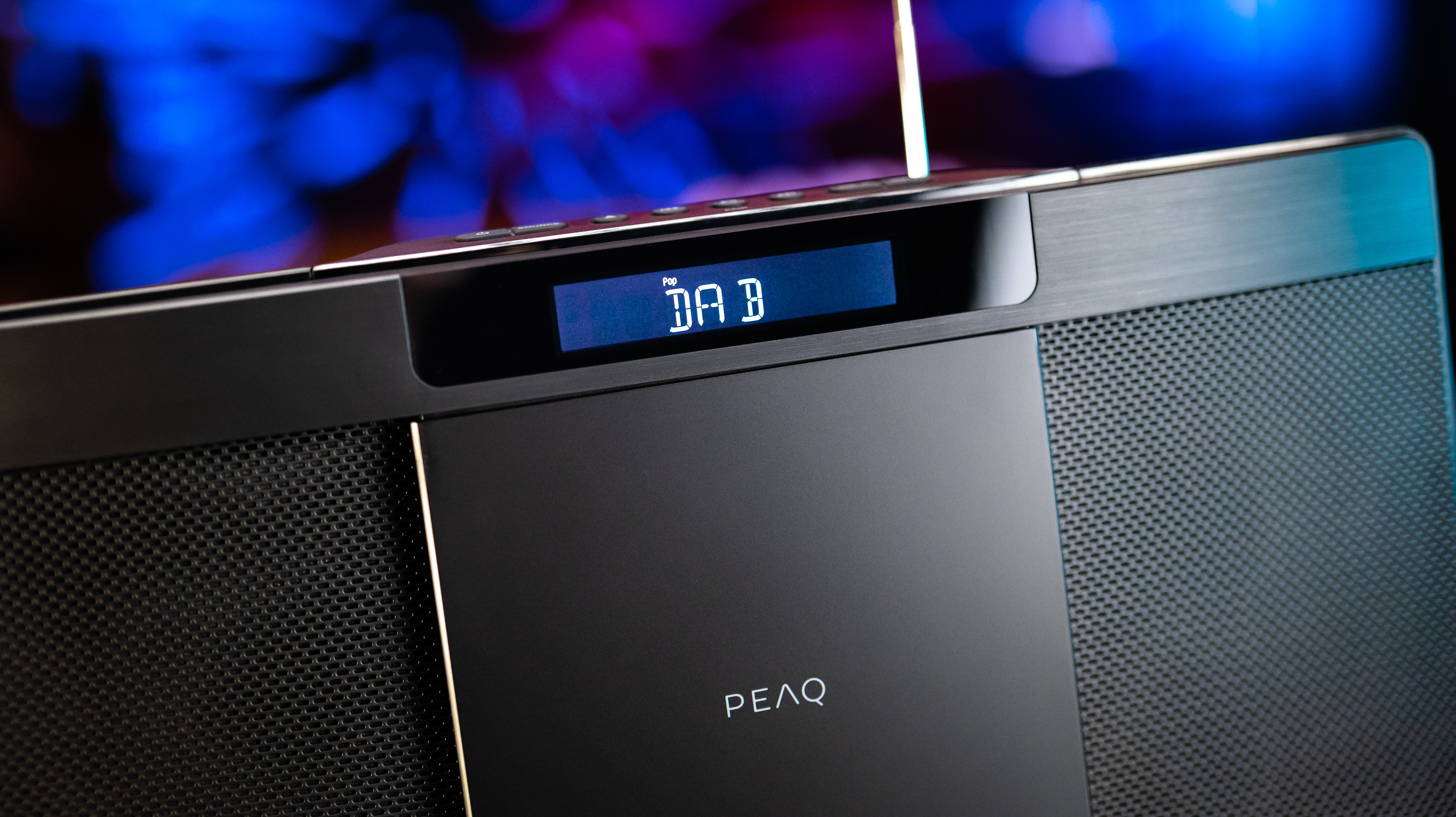 Zbliżenie czarnego stereo z ekranem wyświetlającym „DAB”. Rozmyte niebieskie i fioletowe światła w tle.