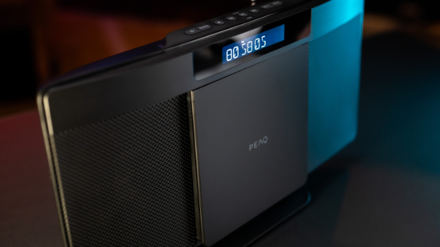 Czarny i srebrny system audio. Wyświetlacz cyfrowy pokazuje czas. Głośniki po bokach, logo Peaq.