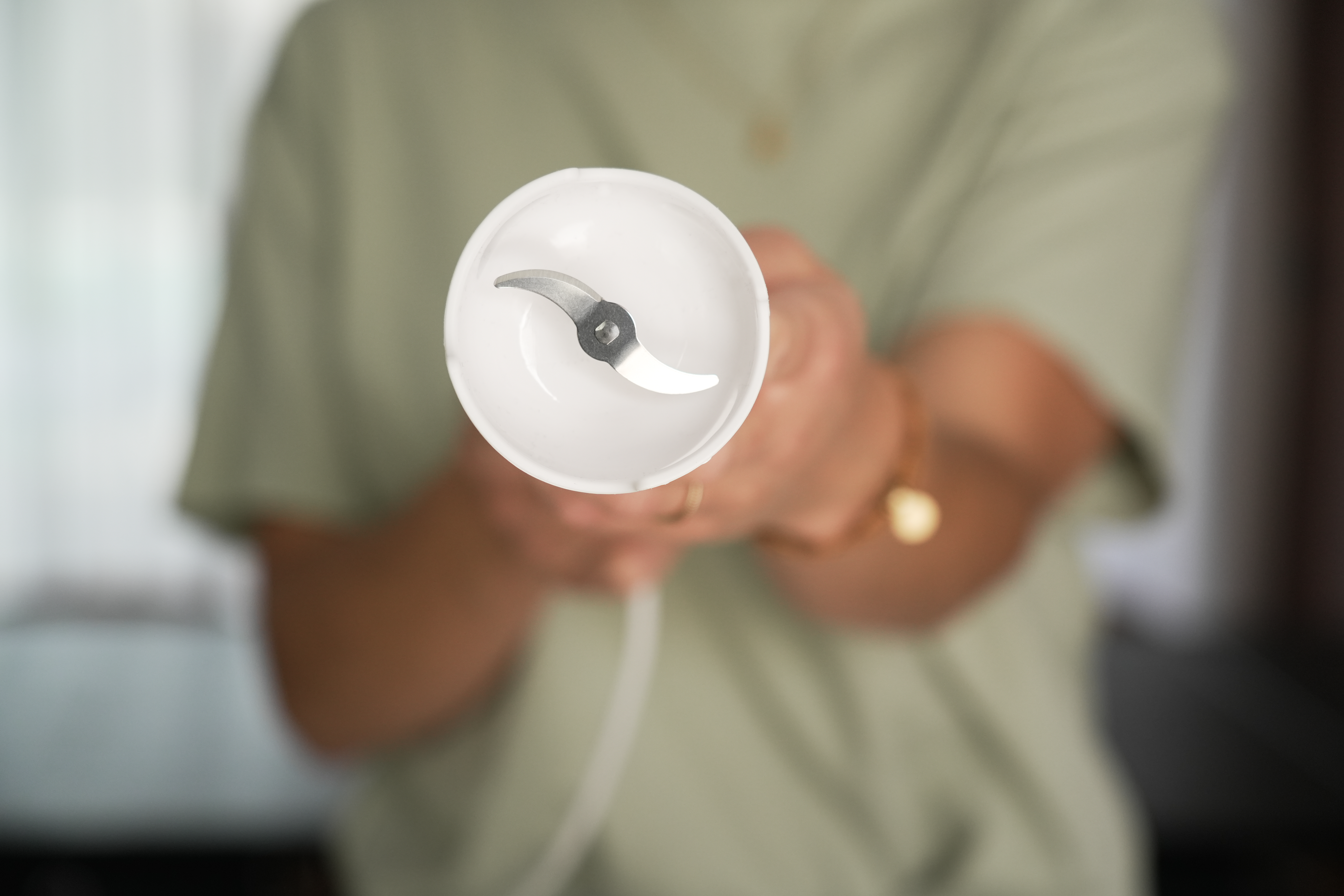 Zbliżenie białego ostrza blendera trzymanego przez osobę w zielonej koszuli.