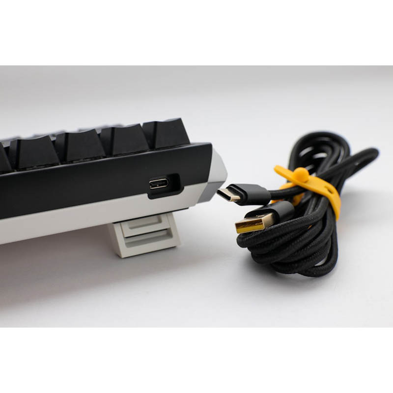 Un teclado blanco y negro con un cable amarillo conectado, sobre fondo blanco.