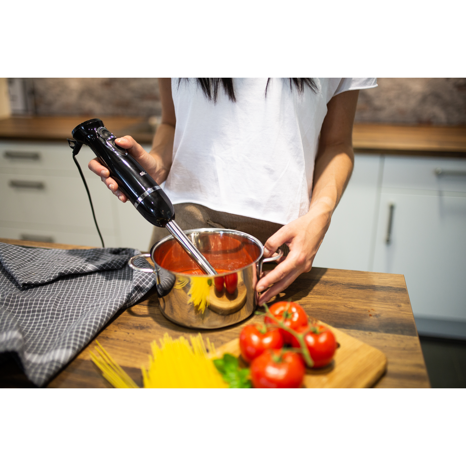 Persoon die tomatensaus mengt in een pan. Tomaten en pasta op hout.