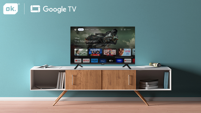 Telewizor na białej szafce na tle turkusowej ściany, z logo Google TV. Pokazuje ekran filmu.