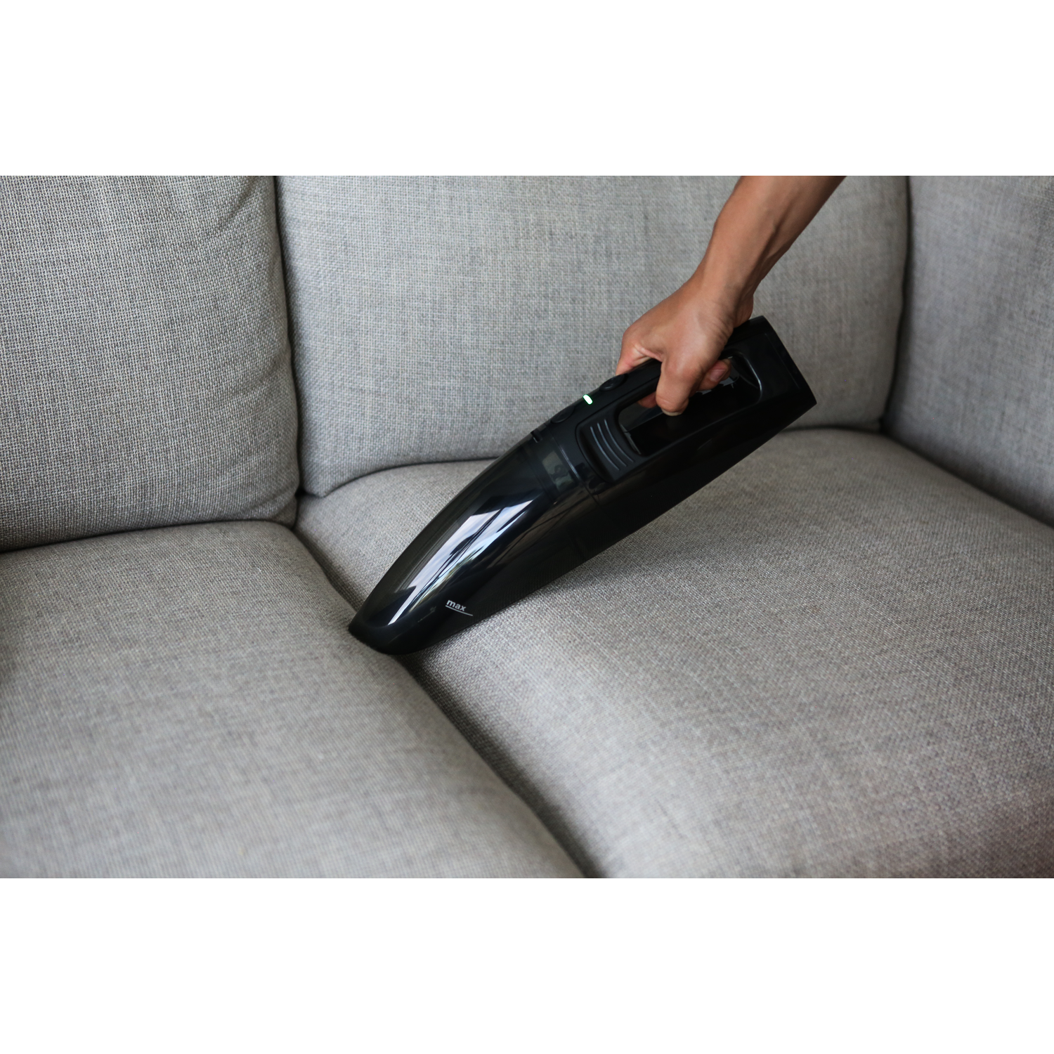 Handheld vacuum cleaner being used on a gray sofa, close up.