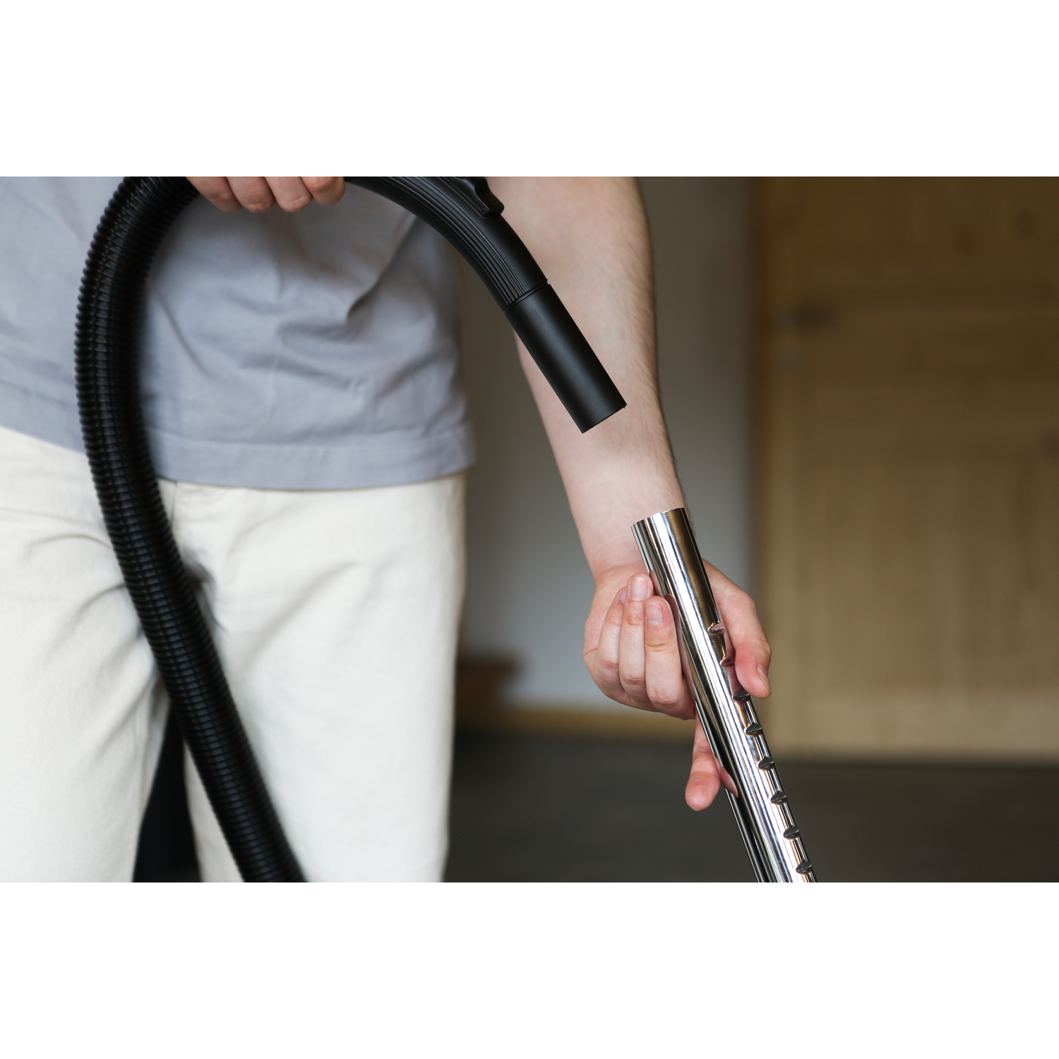 A person is connecting a black hose to a chrome-colored vacuum extension. The background is blurred.