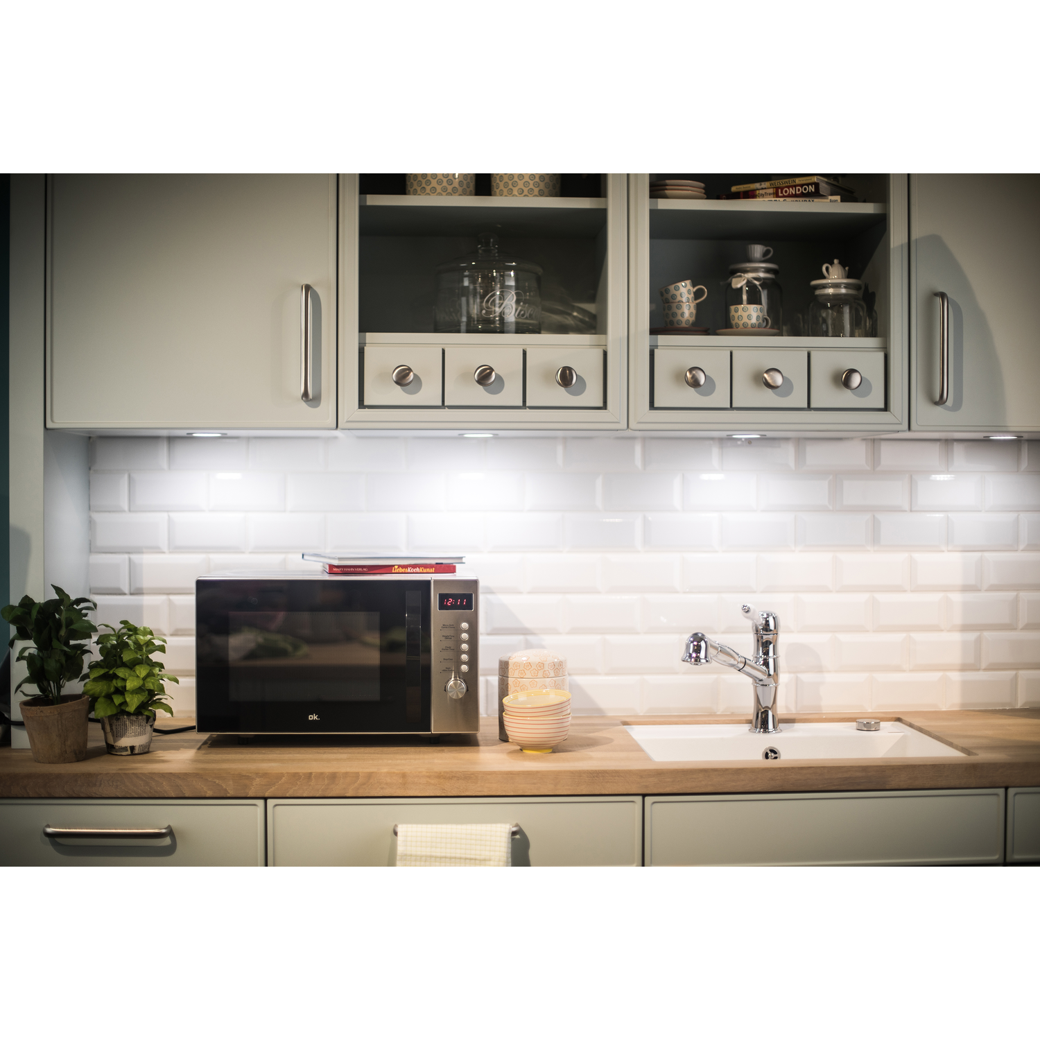 Keuken met magnetron, spoelbak en kasten. Onderkastverlichting is ingeschakeld.