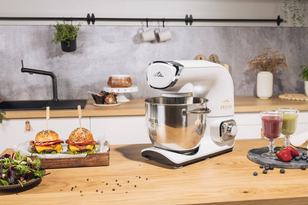 Fehér konyhai mixer, hamburgerek és turmixok a fa pulton.