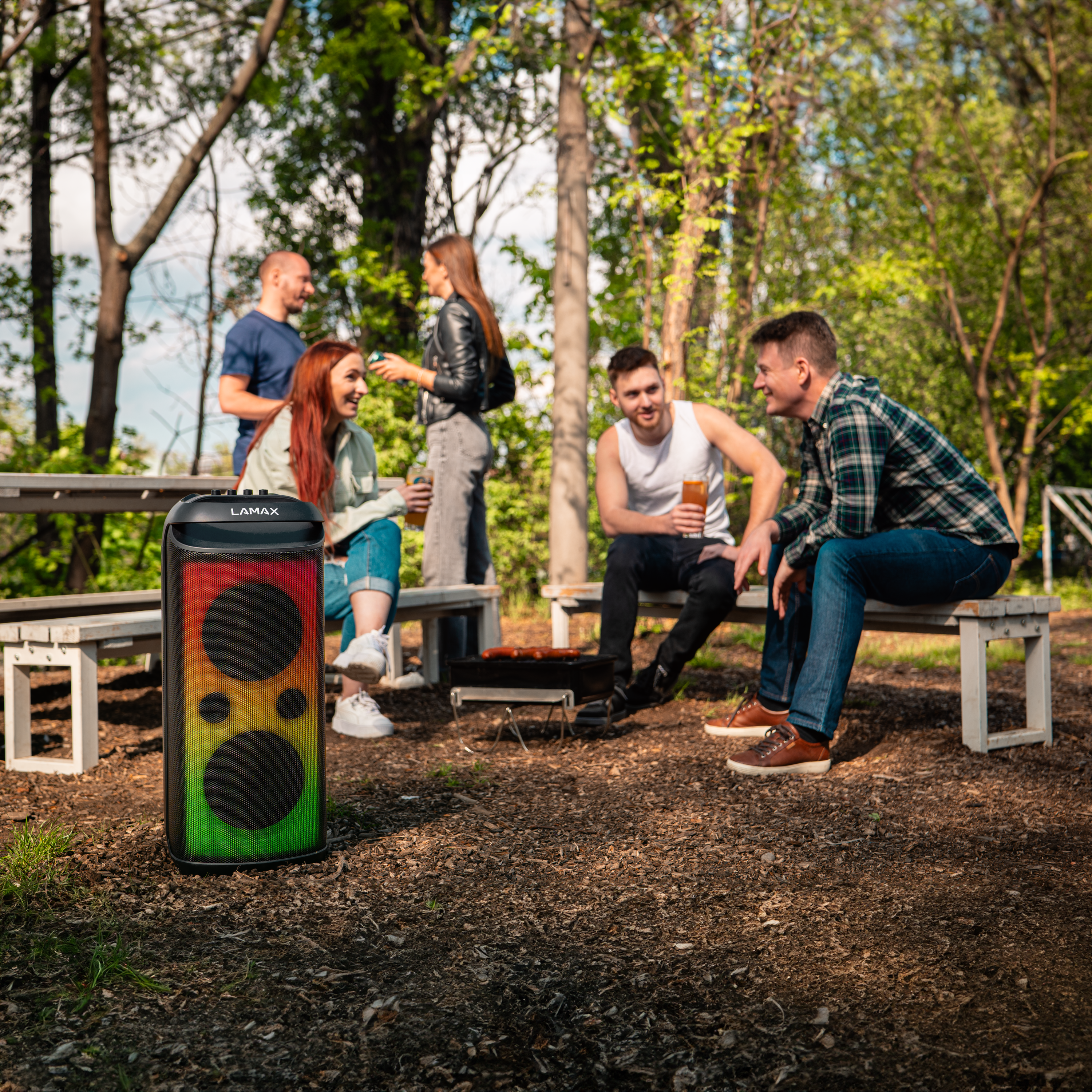 Emberek egy csoportja egy hangszóró körül a parkban. A hangszóró fekete, piros, sárga és zöld.