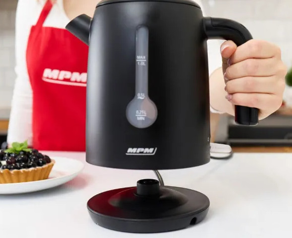 Czarny czajnik elektryczny na stojaku, trzymany przez dłoń.