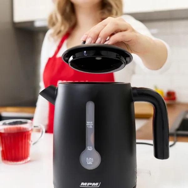 Zbliżenie dłoni otwierającej czarną pokrywę czarnego czajnika elektrycznego.