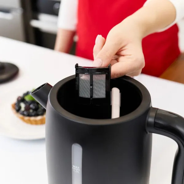 Ręka umieszczająca filtr w czarnym czajniku, z deserem w tle.