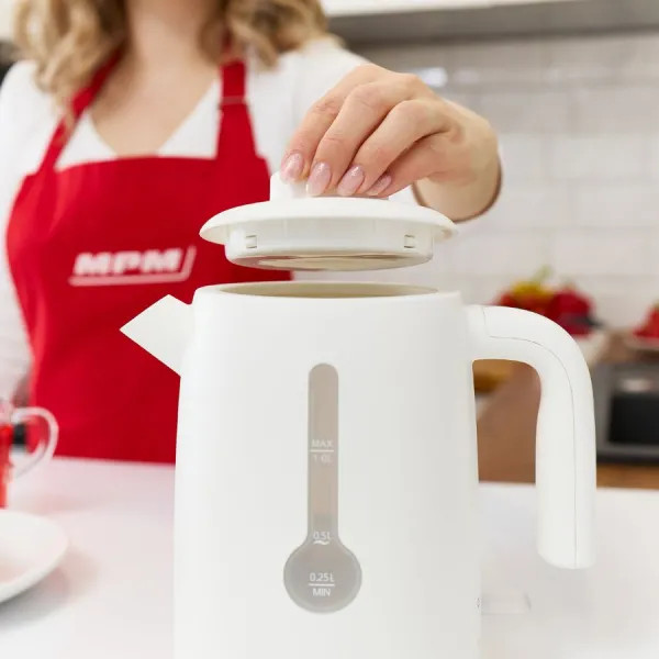 Kobieta otwiera biały czajnik elektryczny. Czerwony fartuch widoczny. Ustawienia kuchni.