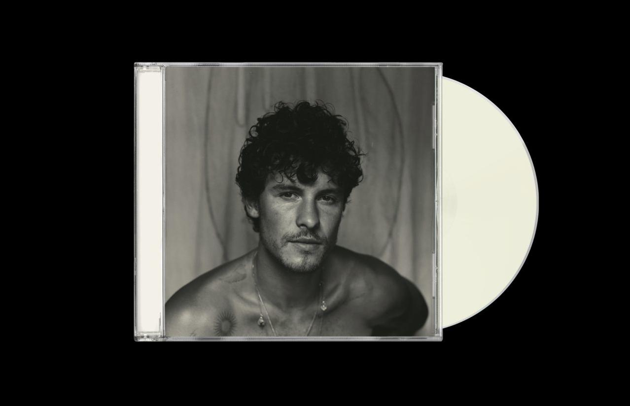 Ein Schwarz-Weiß-Foto eines Mannes ohne Hemd mit lockigem Haar. Er hält eine CD-Hülle und -Scheibe.