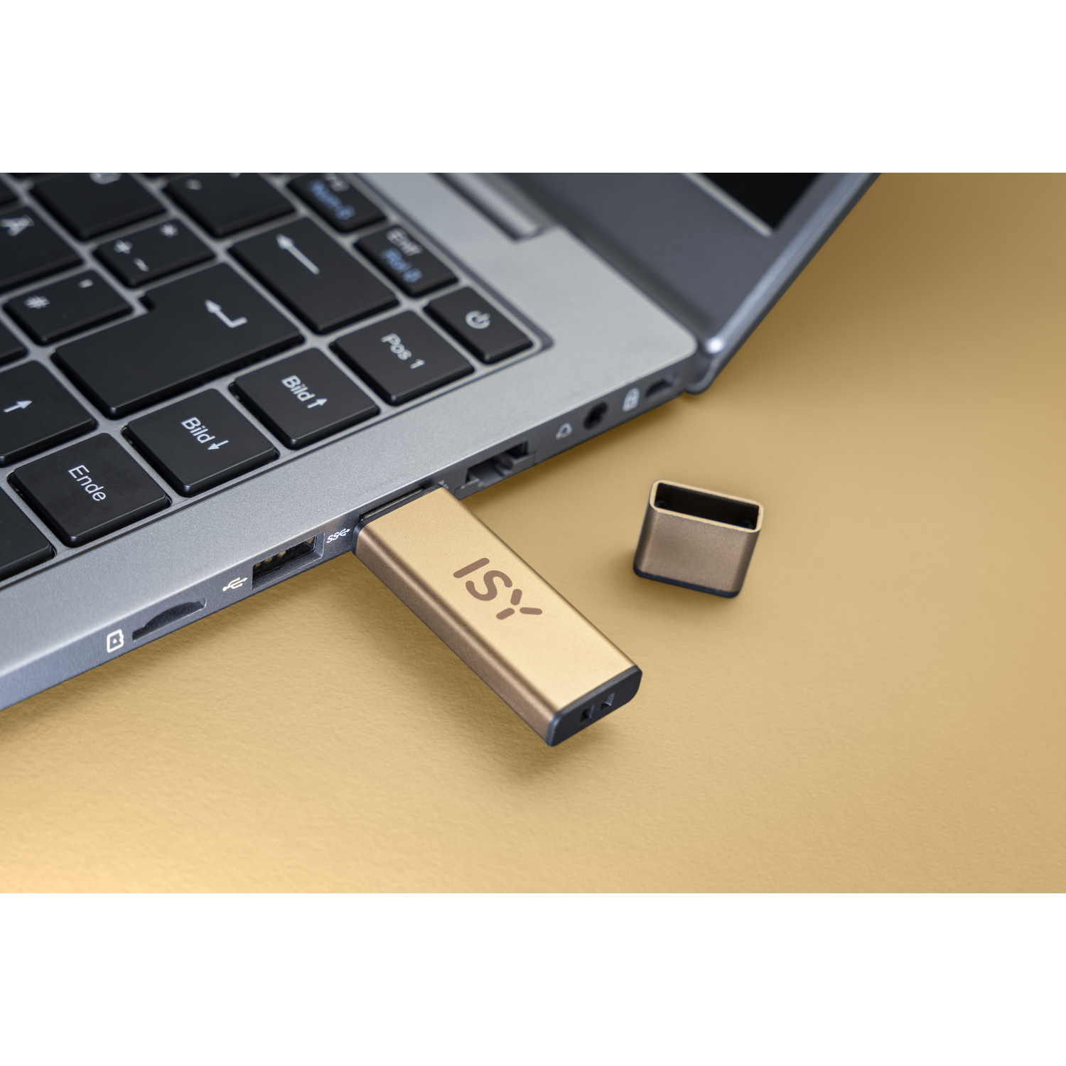 Une clé USB dorée est branchée sur un ordinateur portable, avec un capuchon à côté sur une surface dorée.