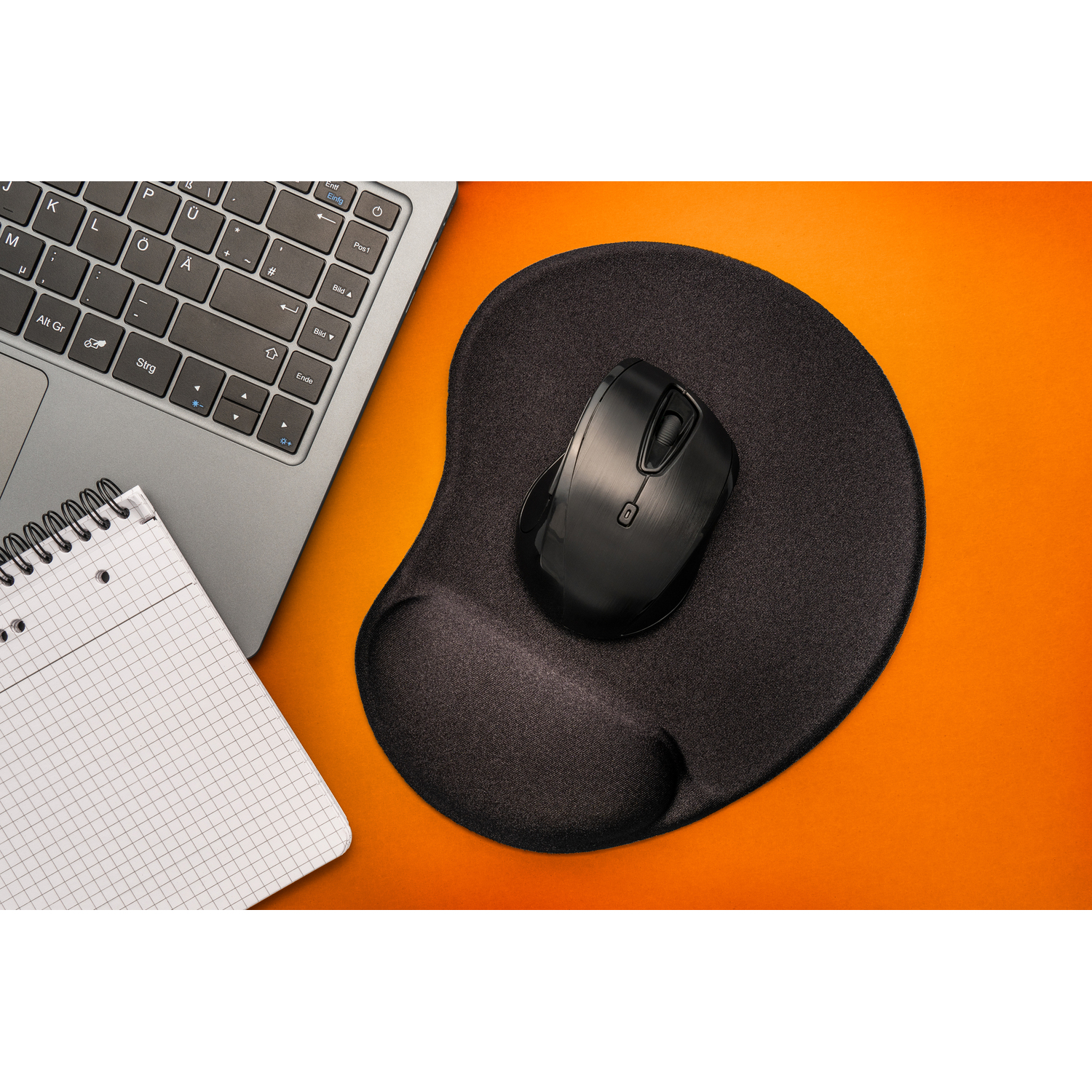 Black mouse on a black ergonomic mousepad and notepad with an orange background. Keyboard in the background.