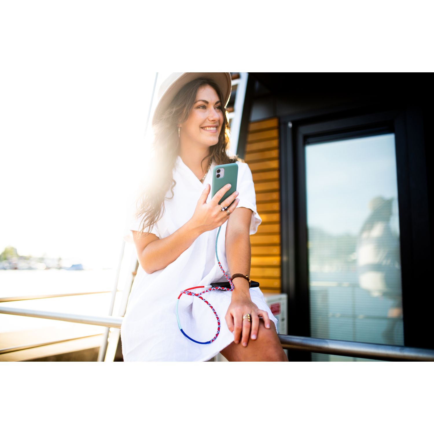 Une femme sourit, tenant un téléphone avec un cordon.