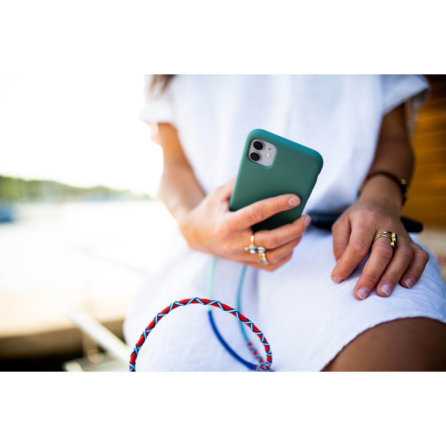 Une personne tenant une coque de téléphone verte, portant une robe blanche et des bagues, près de l'eau.