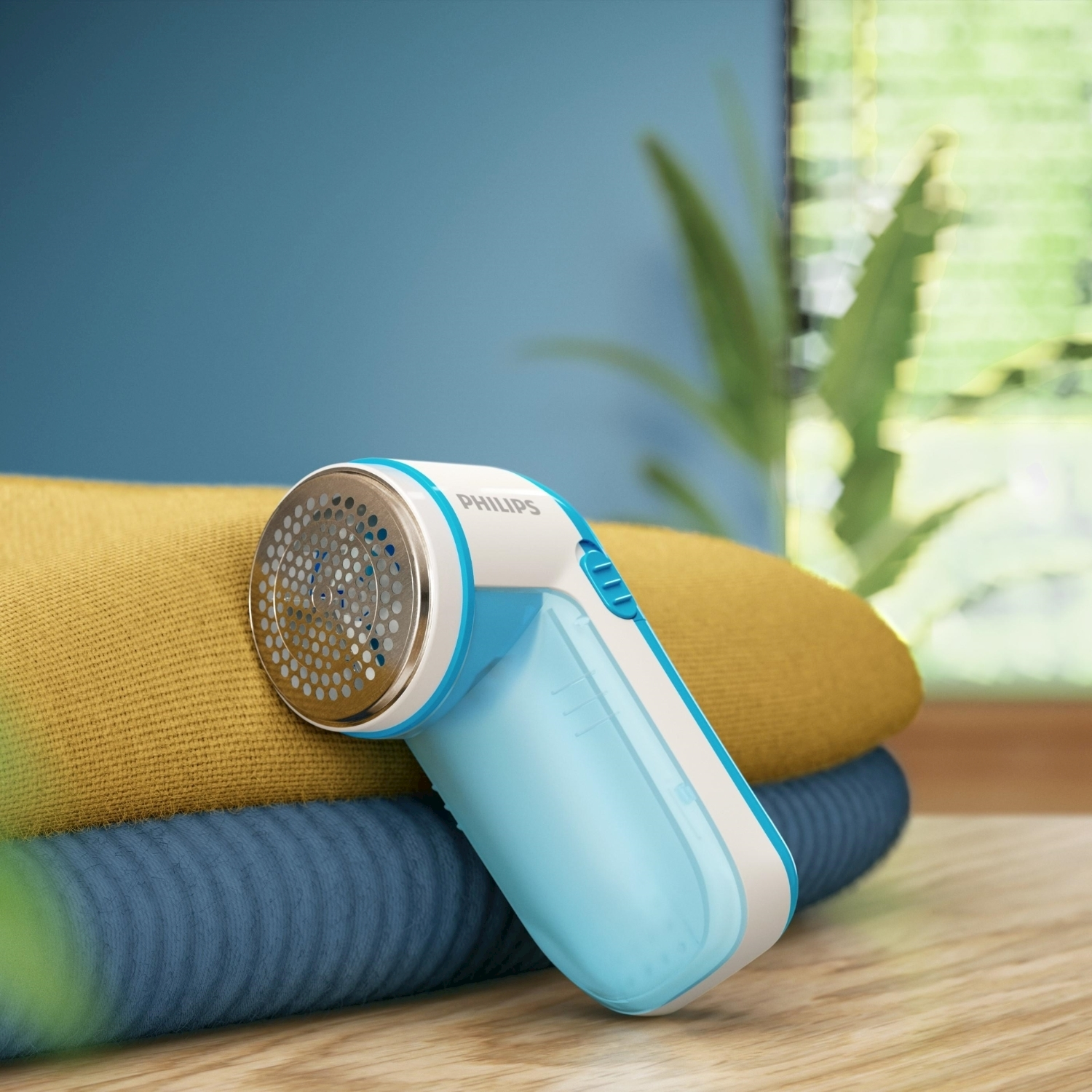 Un rasoio per tessuti Philips blu e bianco su una pila di vestiti piegati, colori giallo e blu.