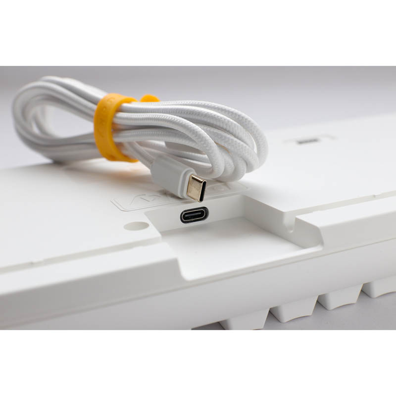 Teclado blanco con cable trenzado blanco y cinta amarilla. Puerto USB-C visible.