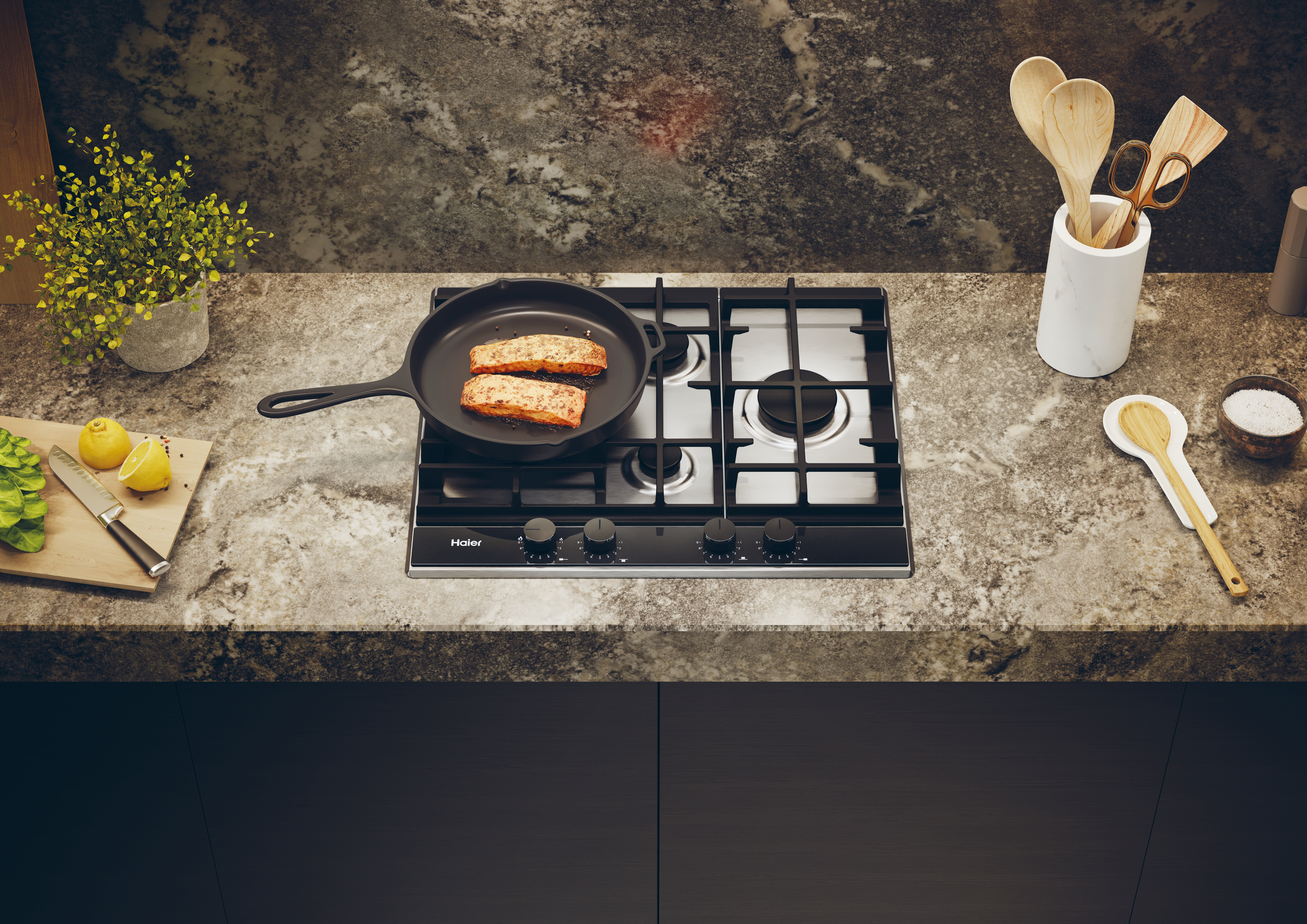 Encimera de cocina con vitrocerámica y comida en sartén. Utensilios varios.