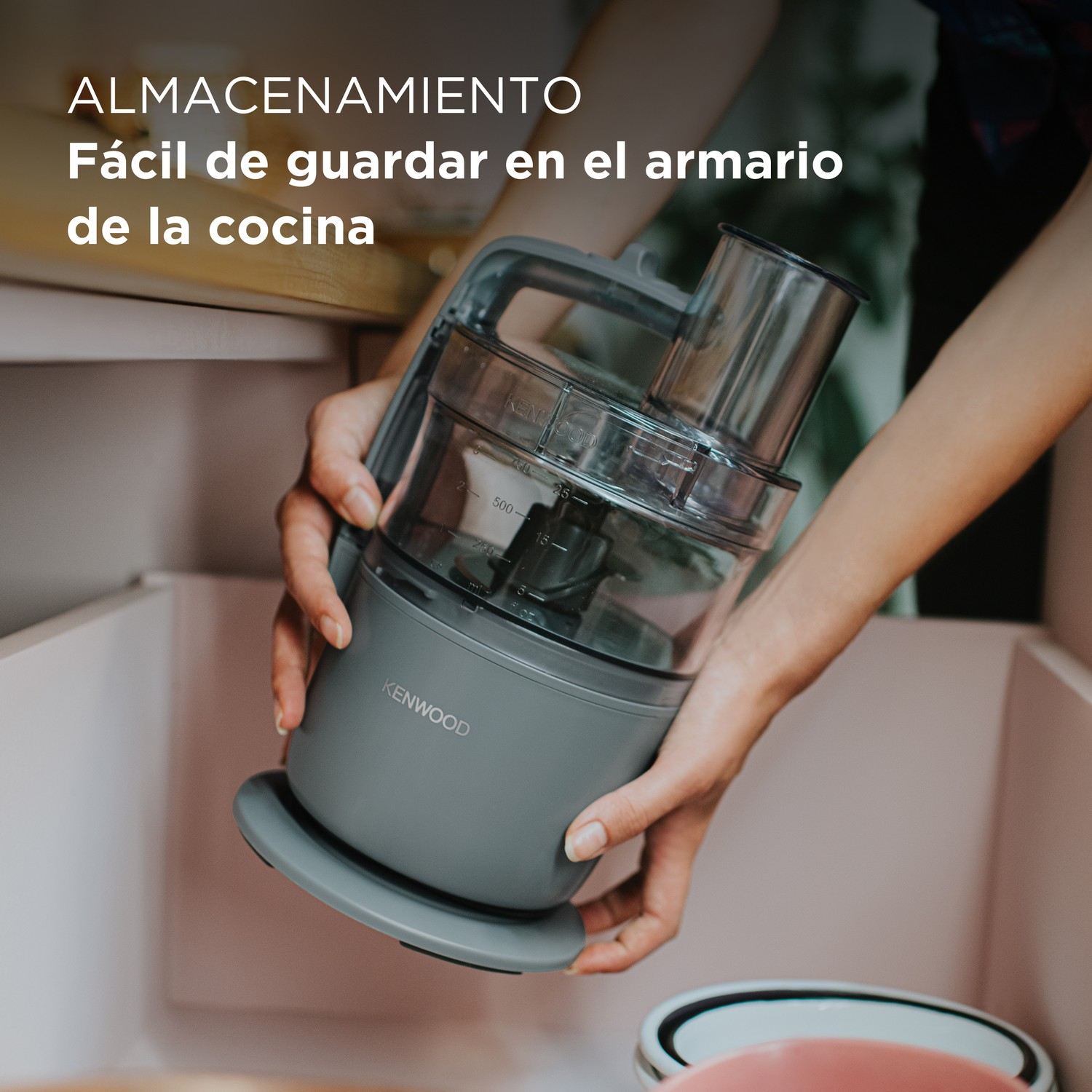 Manos sosteniendo un procesador de alimentos gris, sacándolo de un cajón de cocina con texto: 'Fácil de guardar'.