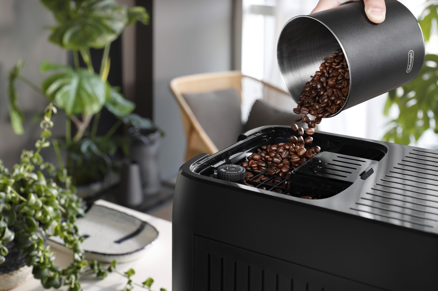 Granos de café se vierten en el recipiente de granos de una cafetera DeLonghi negra.