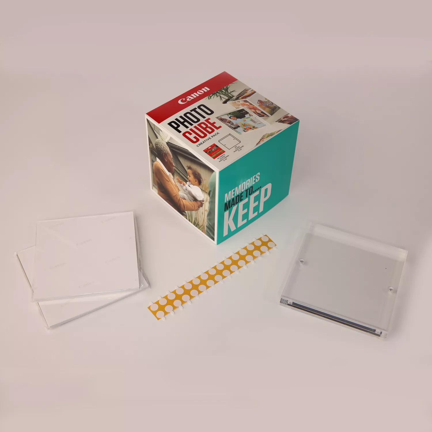 Eine Canon Photo Cube Box mit Zubehör: Fotorahmen, ein Aufkleberstreifen und eine transparente Hülle.