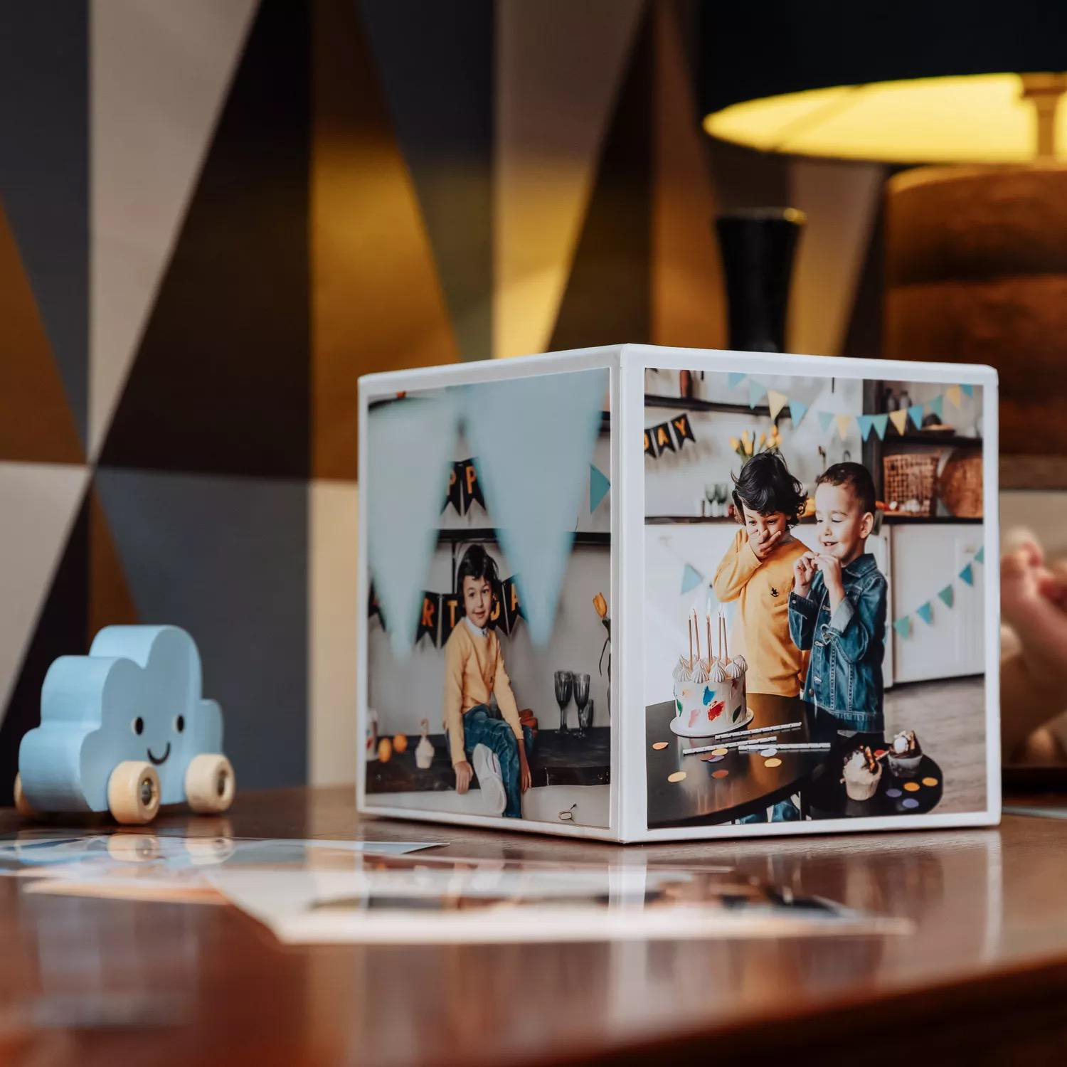 Würfelfotorahmen mit Geburtstagsfotos, Spielzeugauto und Lampe auf einem Tisch.
